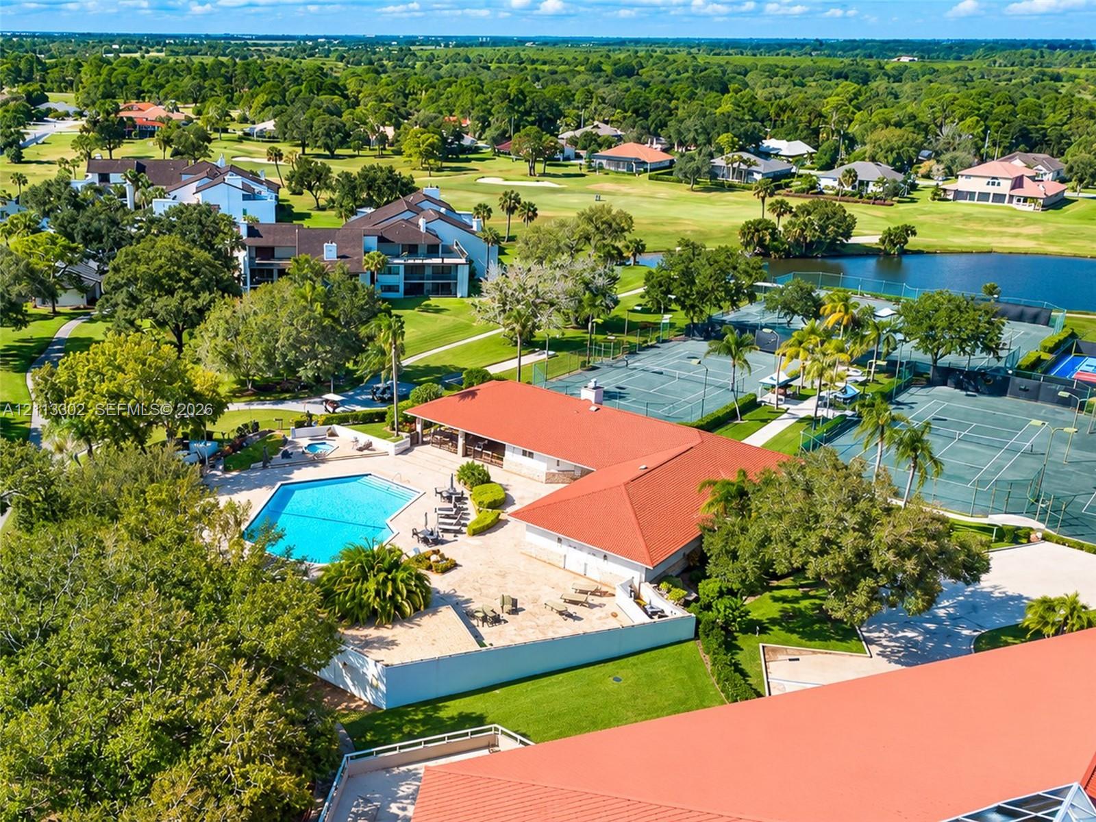 Community recreation center featuring an outdoor swimming pool, multiple tennis courts, a red tile roof, and expansive surrounding lawn areas