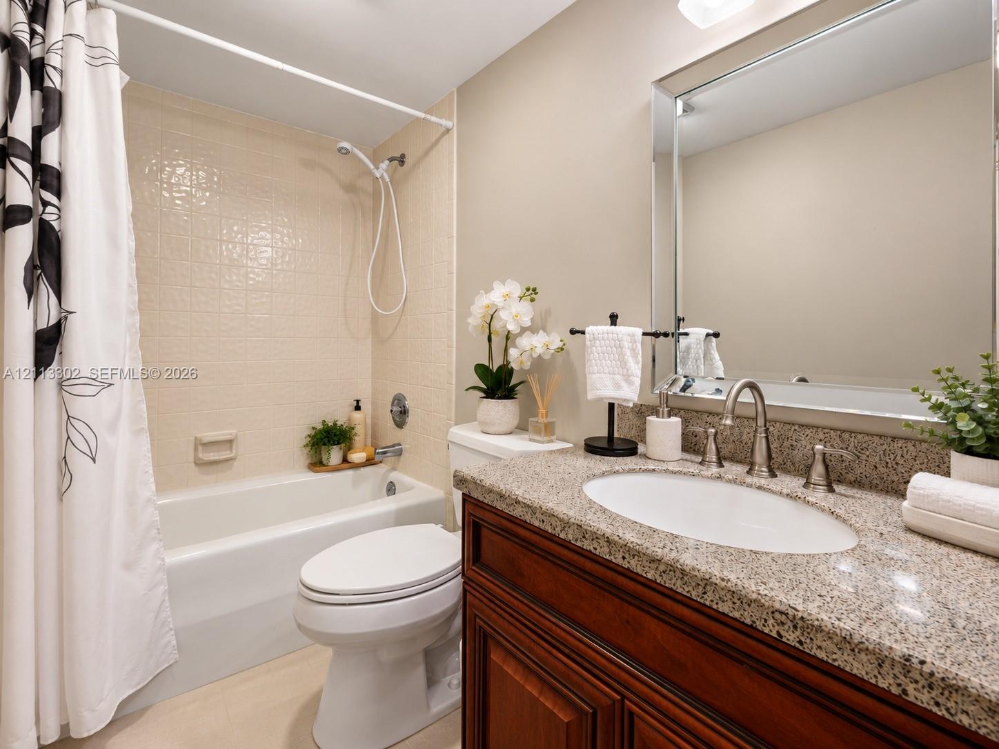 Bathroom featuring a stone-composite countertop, dark wood-finish cabinetry, undermount oval sink, framed wall mirror, and a tiled shower-tub combination with a handheld showerhead