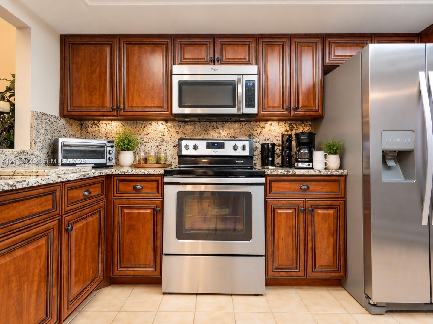 Kitchen featuring stained wood cabinetry, natural stone countertops, tile flooring, and stainless steel appliances including a built-in microwave and range