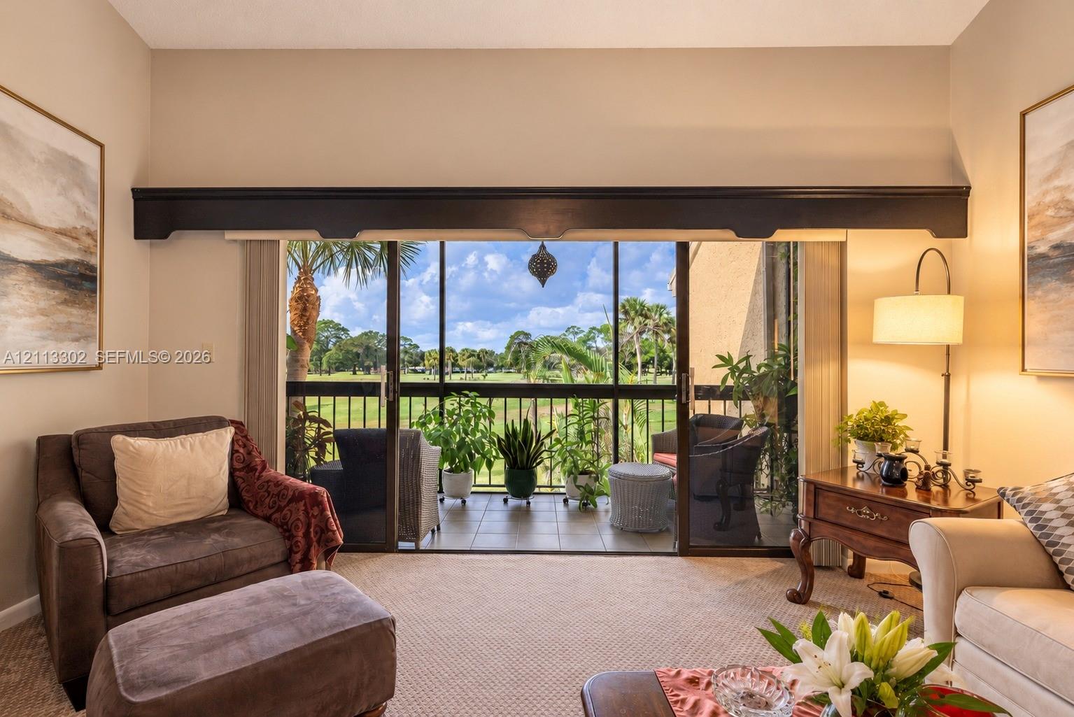 Living space featuring high ceilings, decorative valance, and sliding glass doors leading to a screened balcony with tiled flooring and metal railing