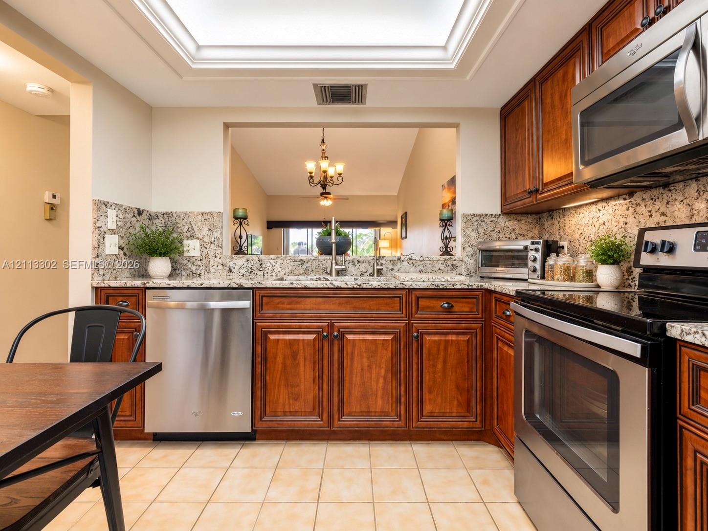 Kitchen featuring wood cabinetry, stone countertops, stainless steel appliances, a recessed skylight, and tile flooring