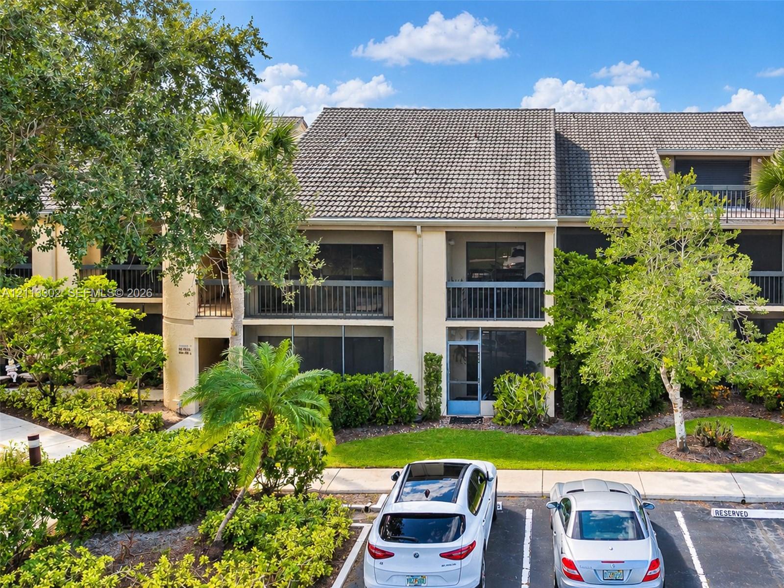 Multi-story building exterior featuring a tile roof, private screened-in balconies, and structured hardscaping surrounded by mature landscaping
