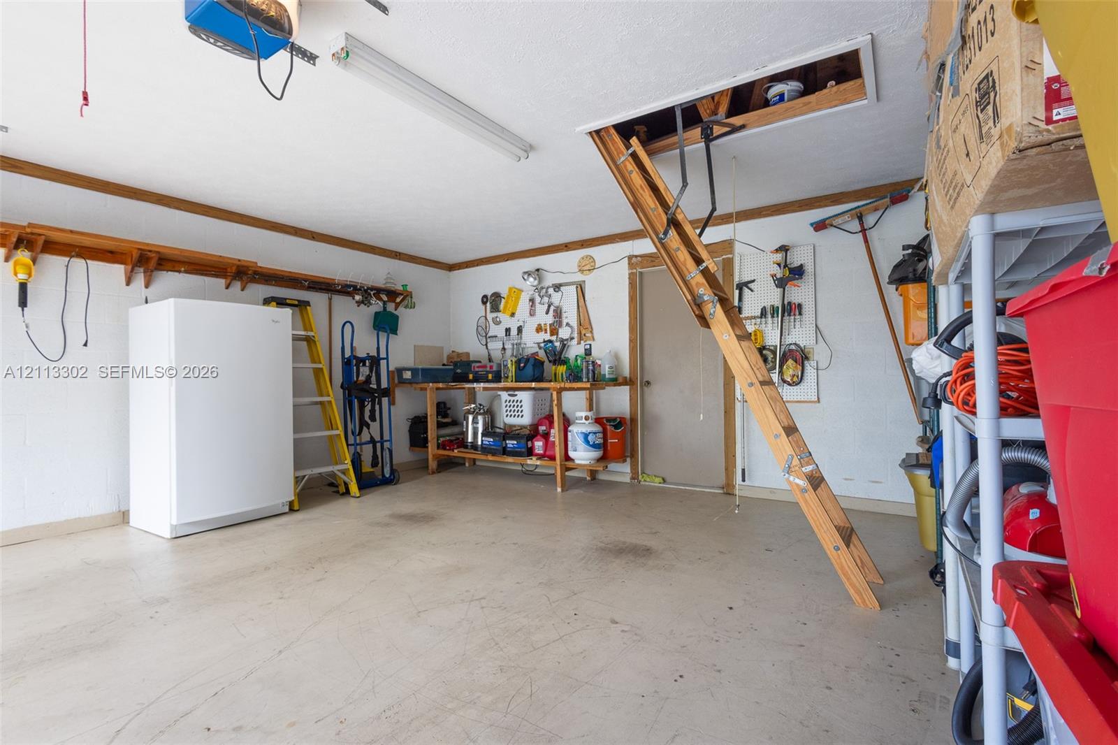 Garage space featuring a pull-down wooden attic ladder, a built-in workbench, overhead fluorescent lighting, and wall-mounted shelving