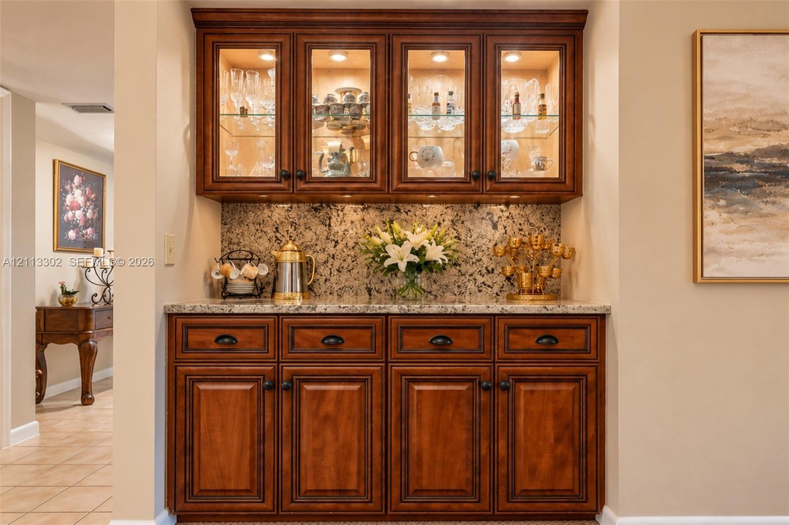Built-in cabinetry featuring rich-toned wood finish, stone-surfaced countertop, glass-front upper cabinet doors, and integrated cabinet lighting