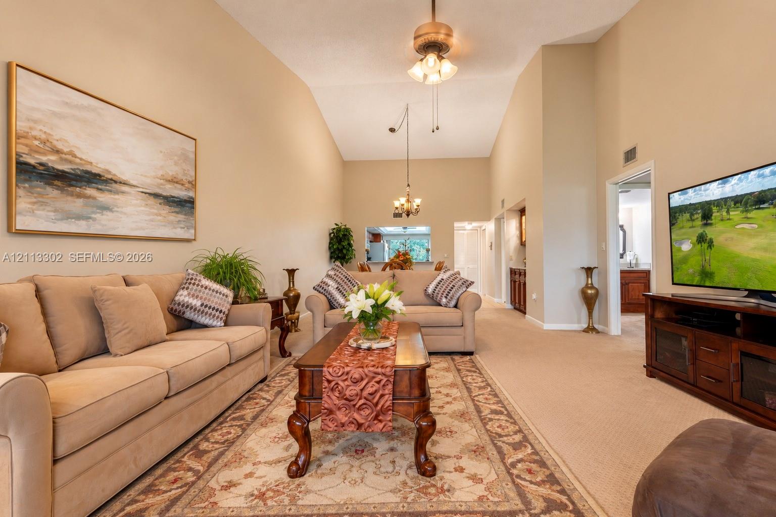 Vaulted ceilings featuring a central ceiling fan and pendant lighting, with a passthrough opening to the kitchen area