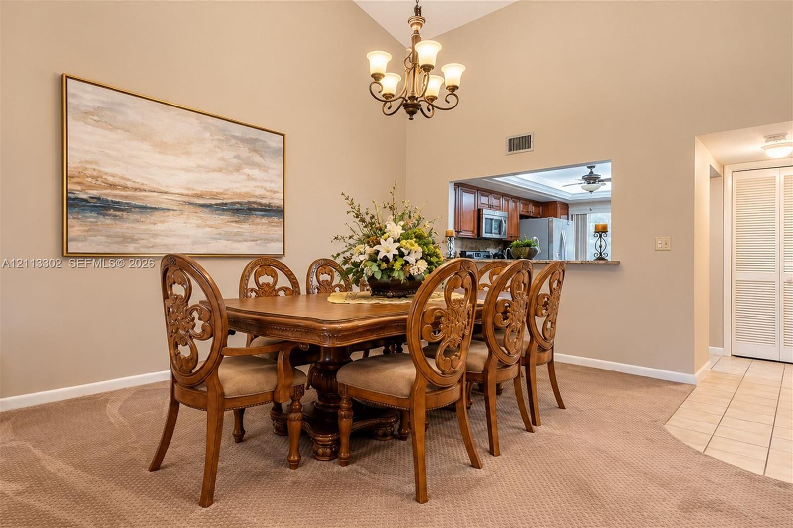 Dining space featuring vaulted ceilings, a multi-arm chandelier, and a serving pass-through opening to the kitchen