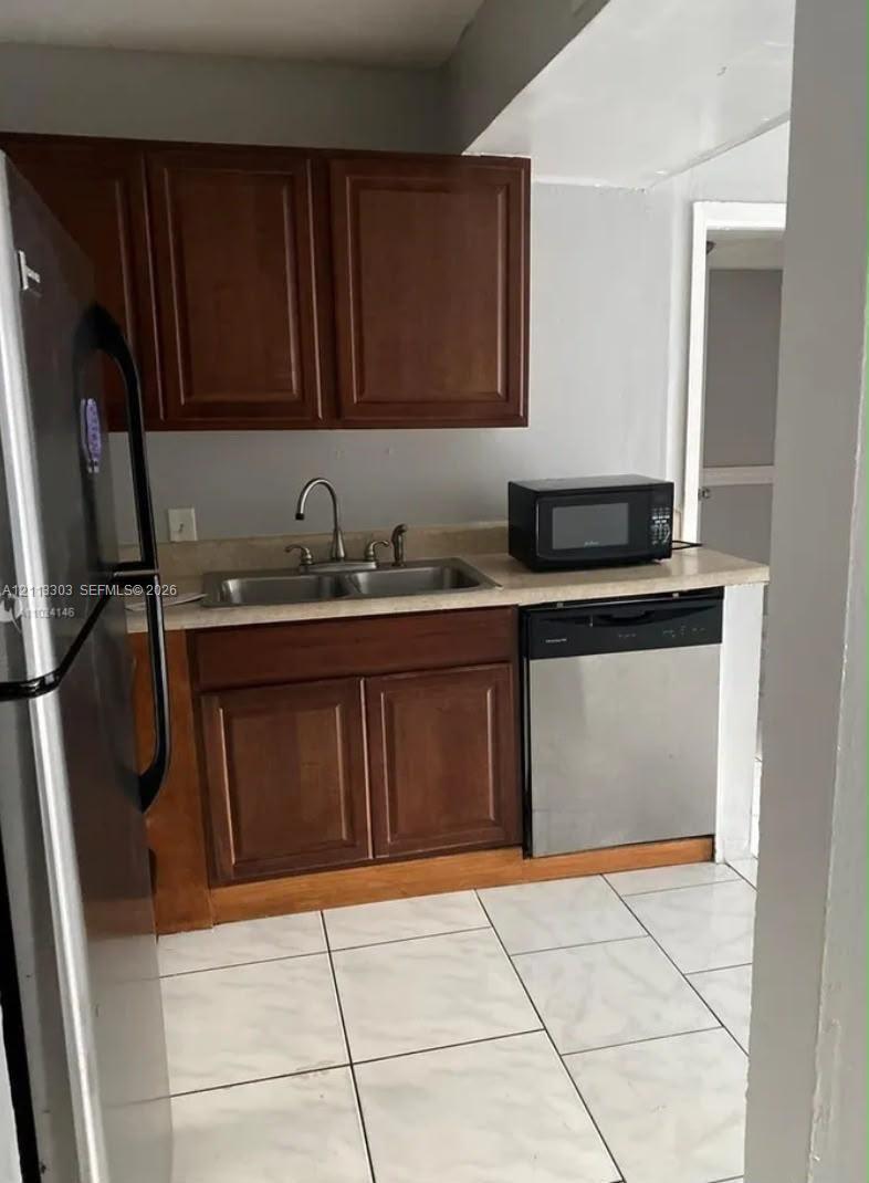 Kitchen featuring wood-finish cabinetry, stainless steel appliances, a double-basin sink, and tile flooring