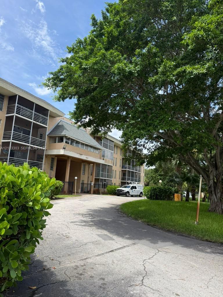 Multi-story exterior featuring screened balconies, shingle roofing, asphalt paving, and mature landscaping
