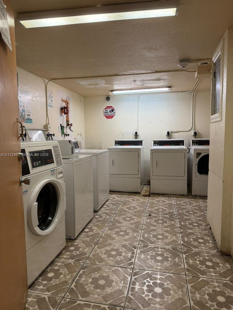 Utility room featuring patterned ceramic tile flooring and multiple white industrial-grade laundry appliances