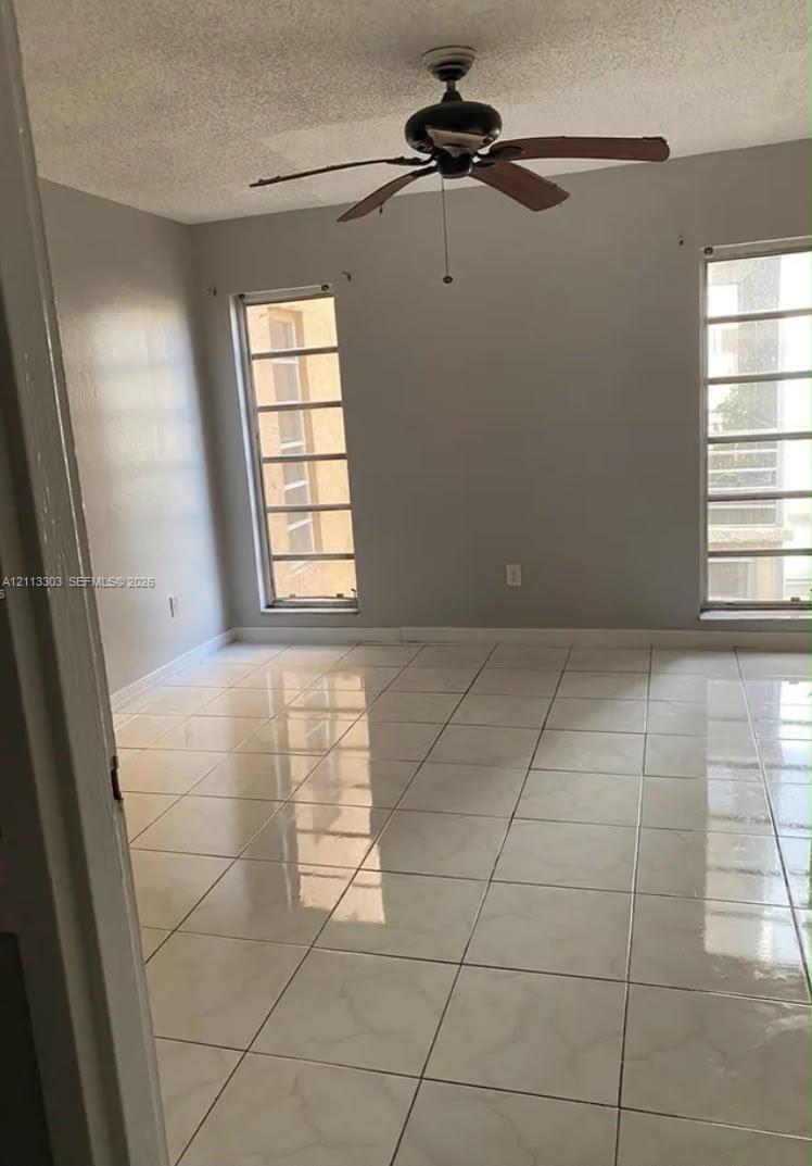 Room interior featuring large-format tile flooring, dual floor-to-ceiling windows with grid muntins, and a central ceiling fan