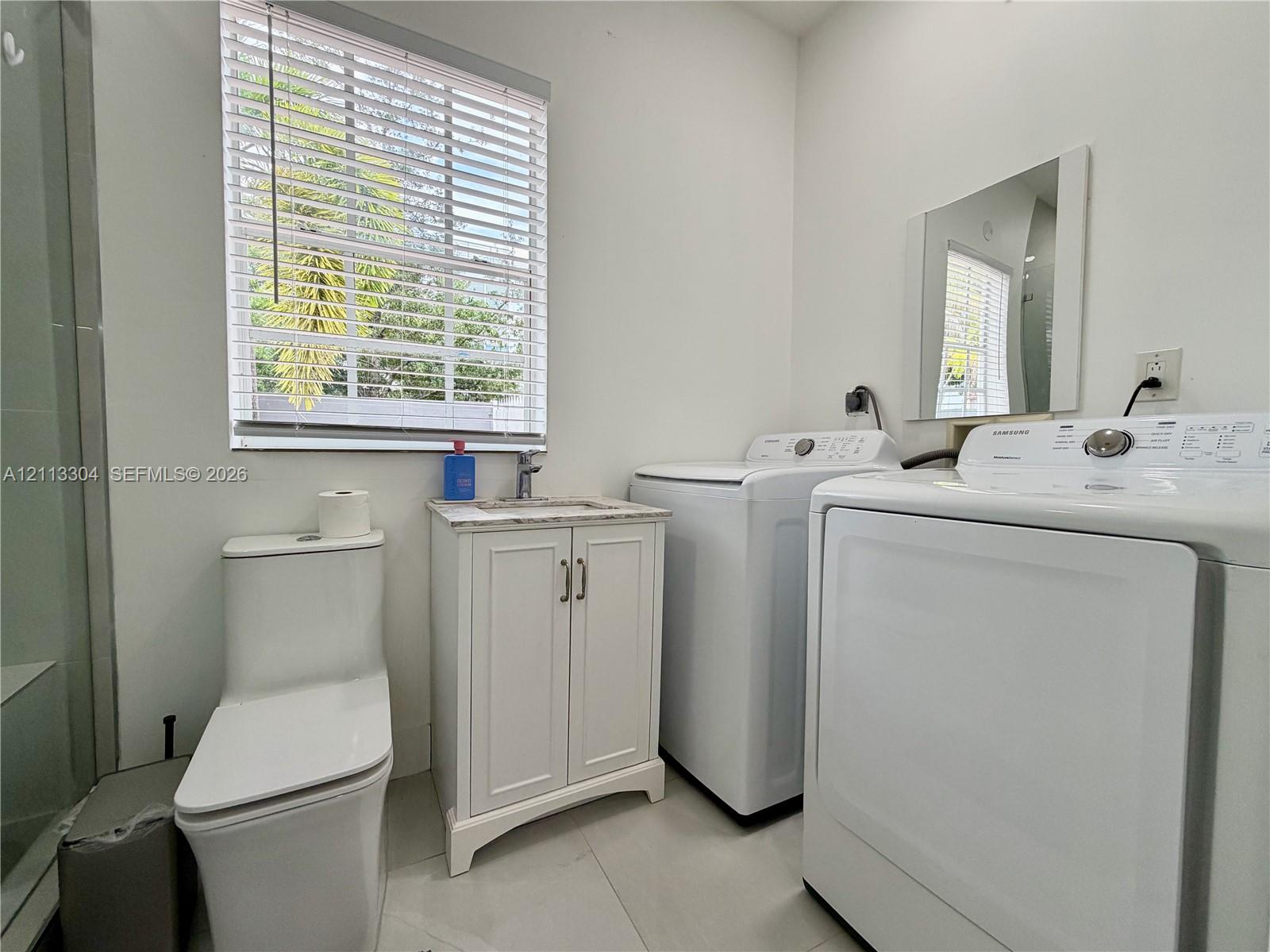 Bathroom featuring a floor-mounted toilet, vanity with a stone-finish countertop and integrated sink, wall-mounted mirror, and tile flooring