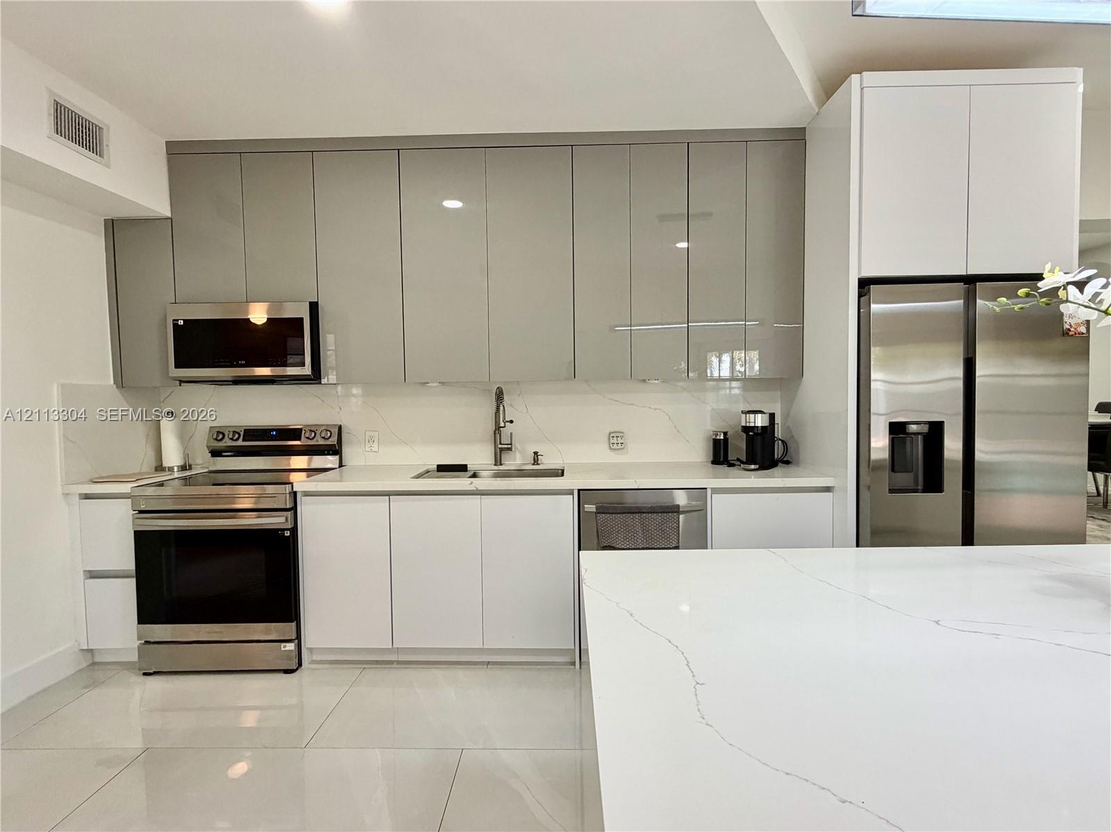Kitchen featuring high-gloss cabinetry, stone-finish countertops with matching backsplash, stainless steel appliances, and large-format tile flooring