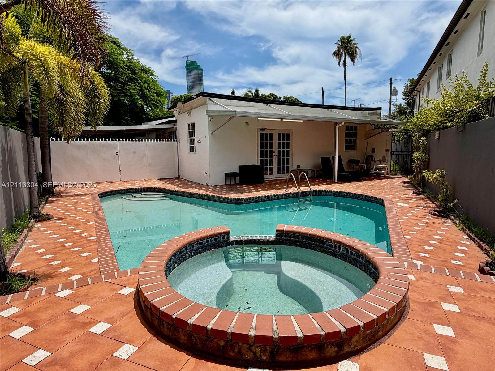 Private outdoor area featuring an in-ground swimming pool, raised circular spa with tile finish, expansive tiled patio, and solid white fencing