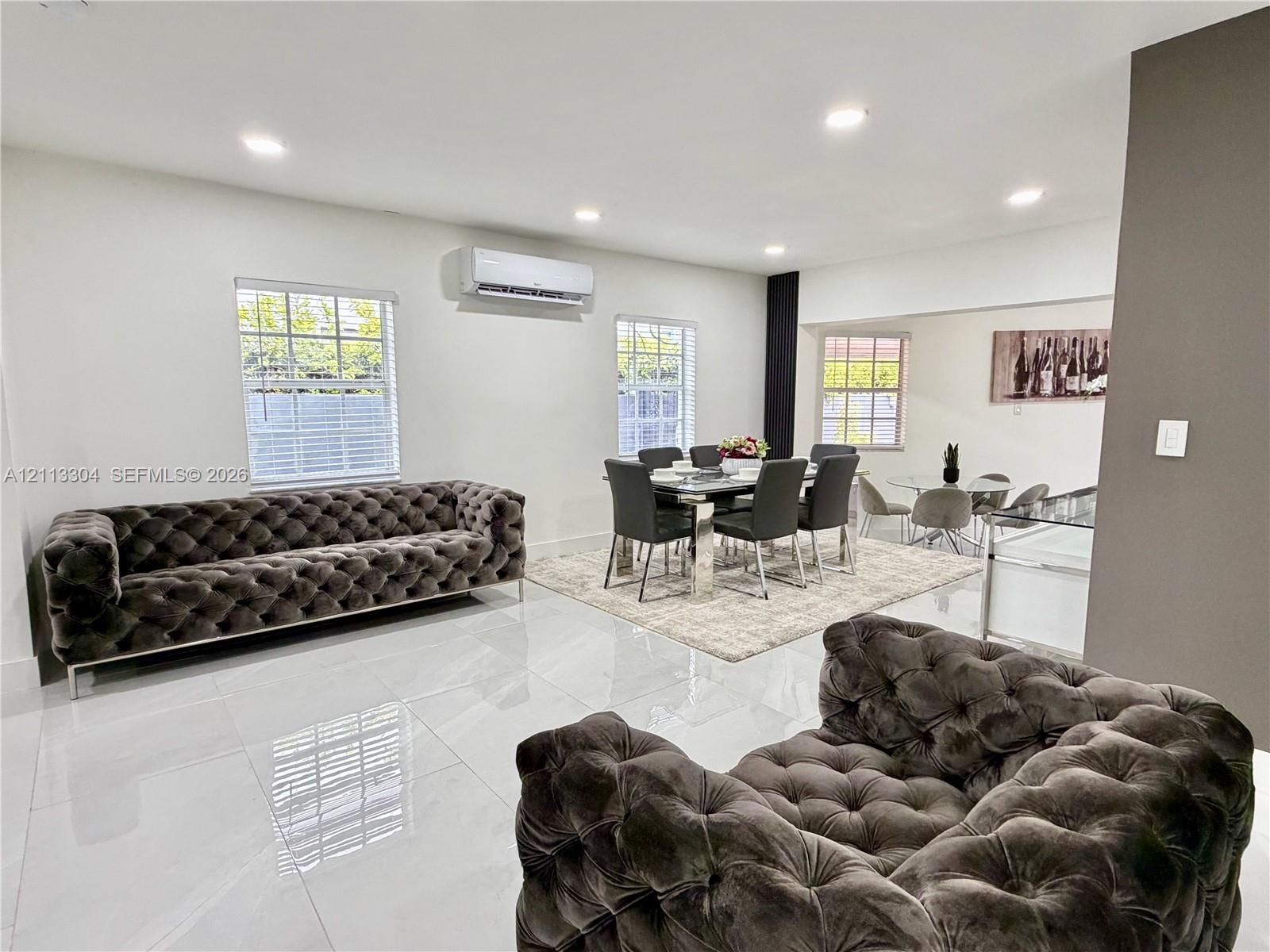 Large-format tile flooring, recessed ceiling lighting, wall-mounted ductless air conditioning unit, and multiple windows with white blinds