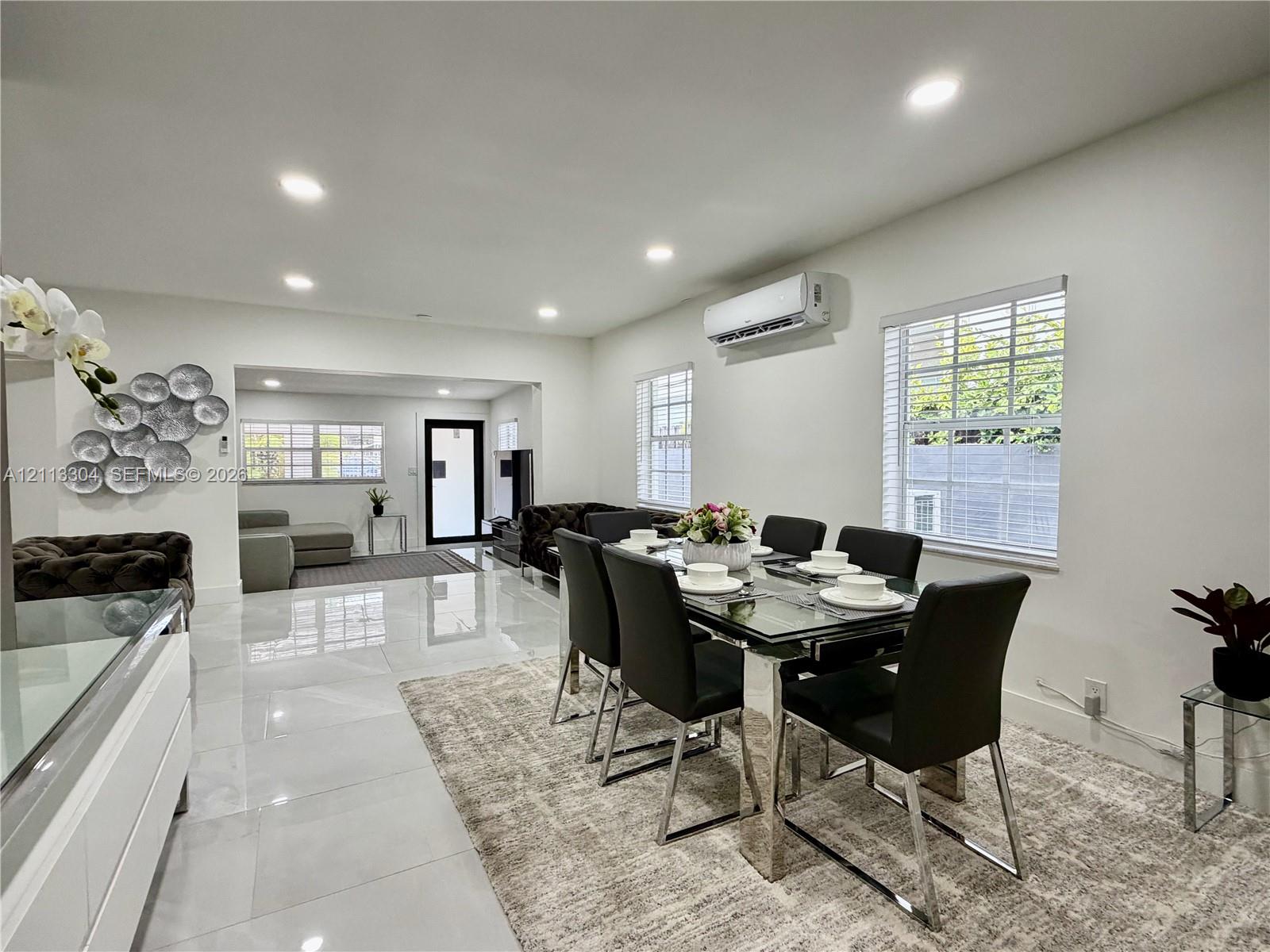 Polished tile flooring, recessed lighting, wall-mounted climate control unit, and multiple windows with white horizontal blinds