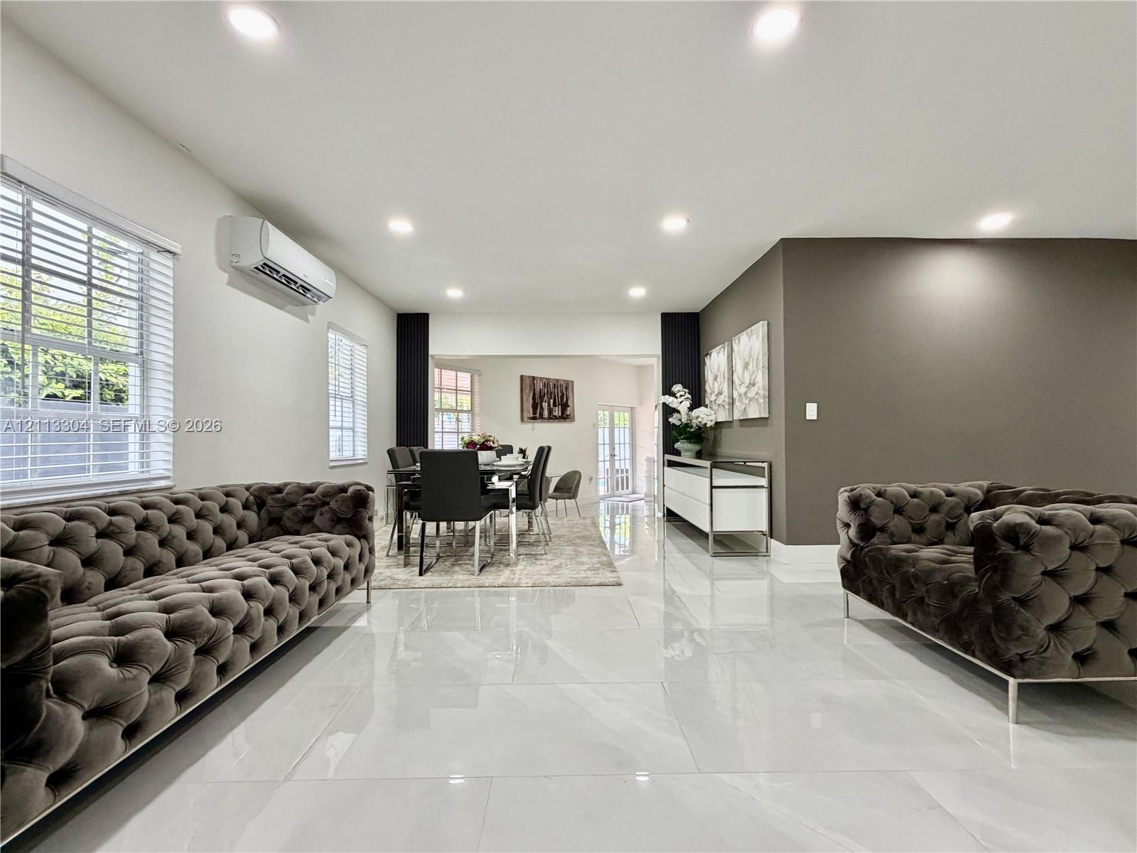Large-format polished tile flooring, wall-mounted ductless climate control unit, recessed lighting, and accent wall featuring a neutral color palette