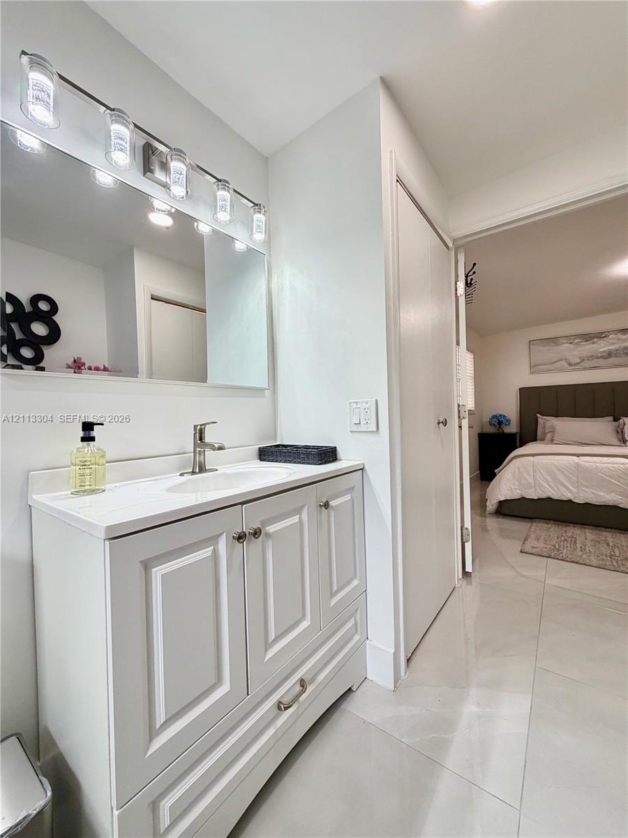 White vanity with shaker-style cabinetry, solid-surface countertop with an integrated sink, polished metal hardware, and a multi-bulb light fixture mounted above a rectangular mirror