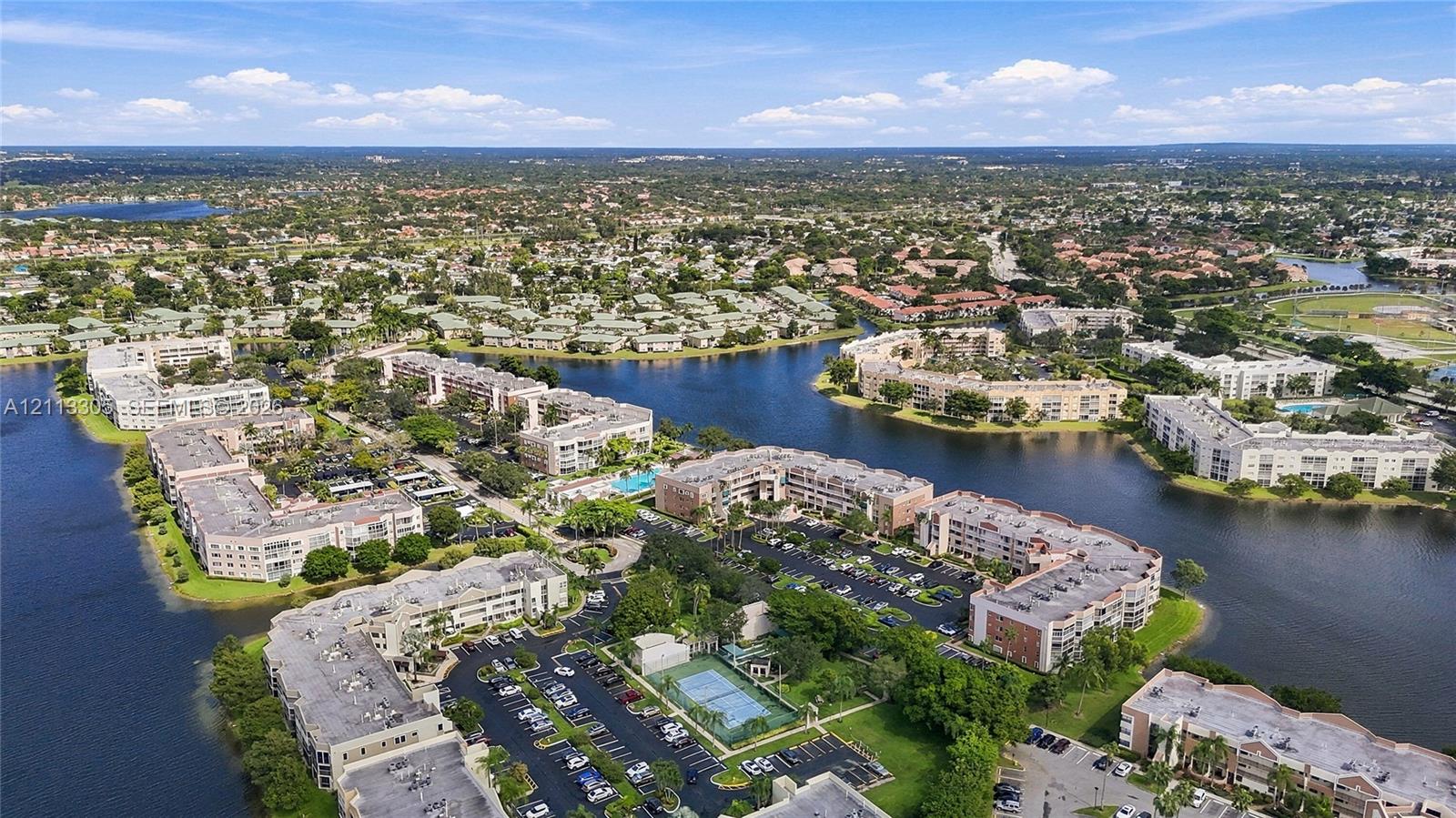 Aerial perspective featuring multi-story residential buildings, water frontage, tennis courts, and dedicated surface parking