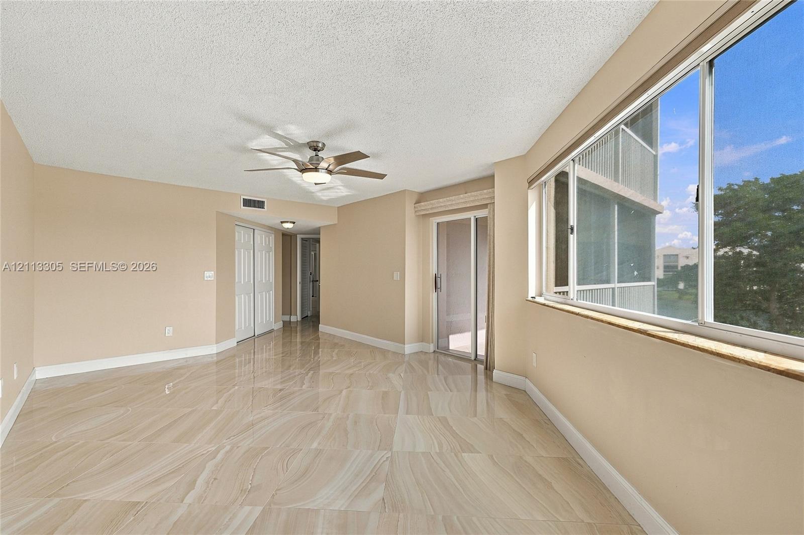 Polished stone-finish tile flooring, large sliding glass door, oversized windows with a stone-top sill, and a multi-blade ceiling fan