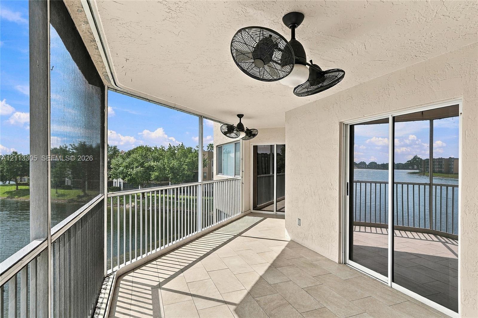 Screened balcony featuring tile flooring, metal railings, dual ceiling-mounted fans, and sliding glass doors