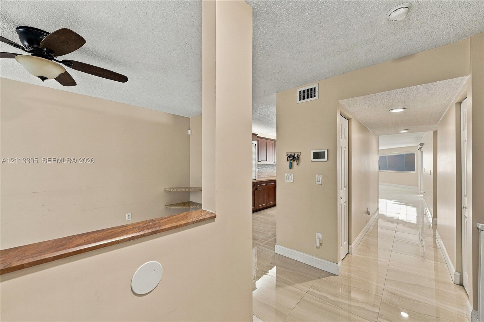 Polished tile flooring, neutral wall tones, wooden ceiling fan with integrated lighting, wood-capped half-wall partition with built-in shelving, and recessed ceiling lighting