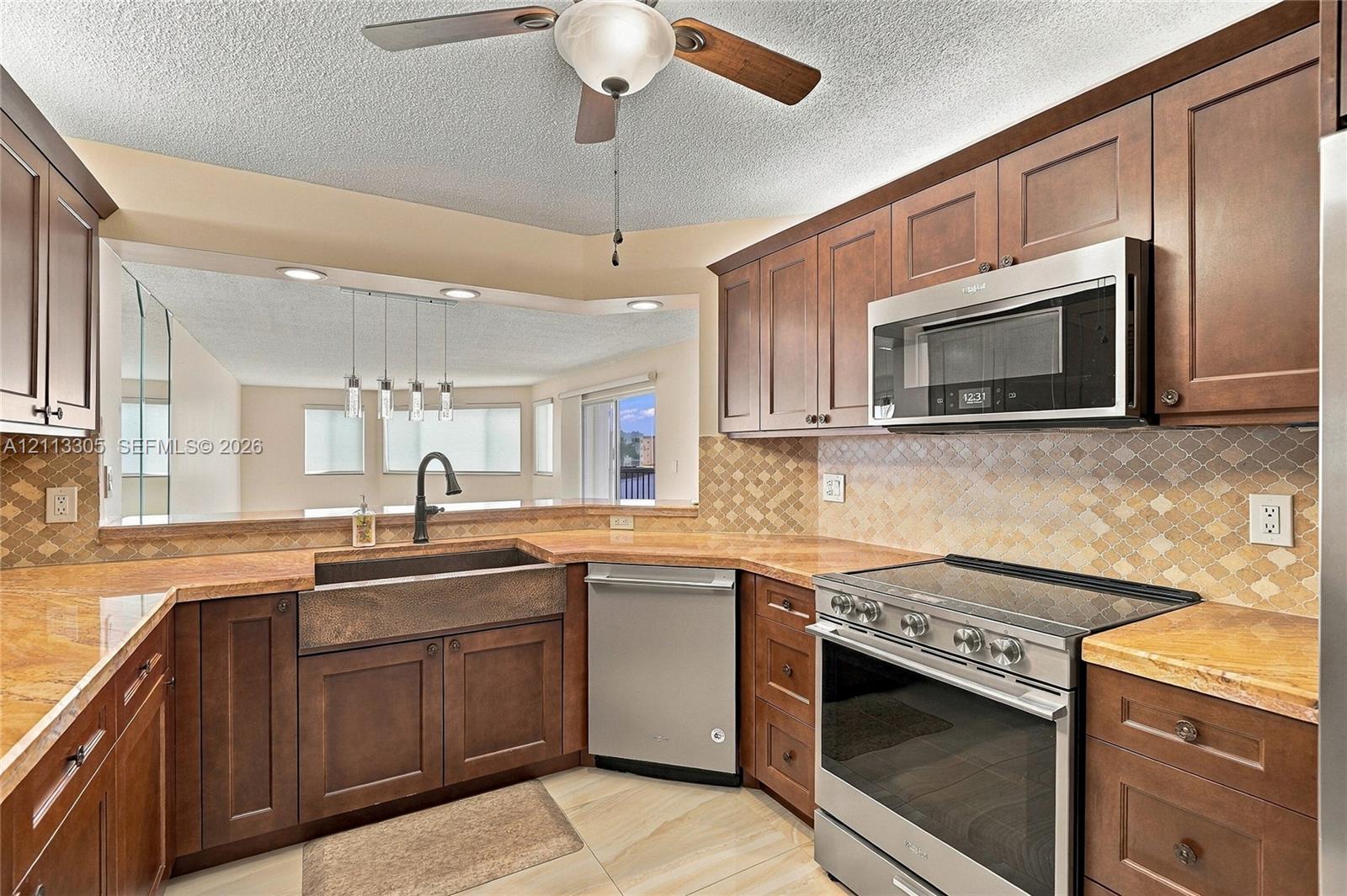 Kitchen featuring dark wood cabinetry, stone-finish countertops, stainless steel appliances, a farmhouse sink with a gooseneck faucet, and a decorative tile backsplash
