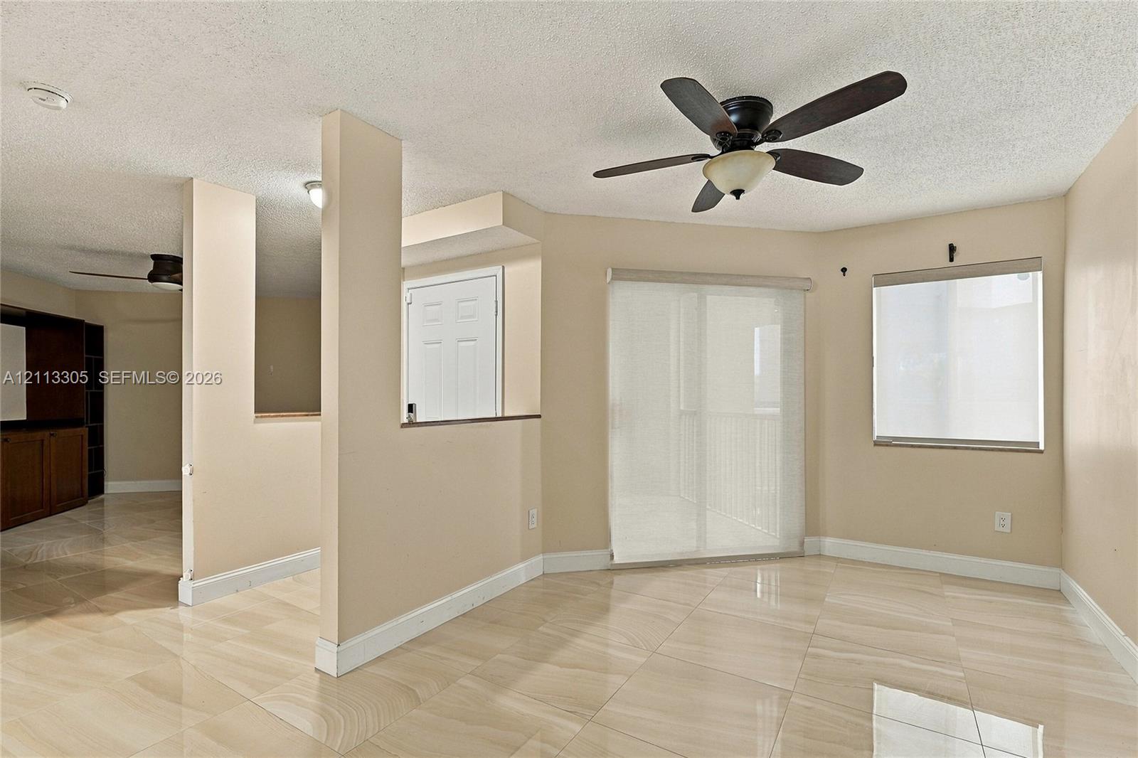 Neutral-toned interior space featuring polished tile flooring, a multi-blade ceiling fan with integrated lighting, sliding glass patio doors, and a partial partition wall