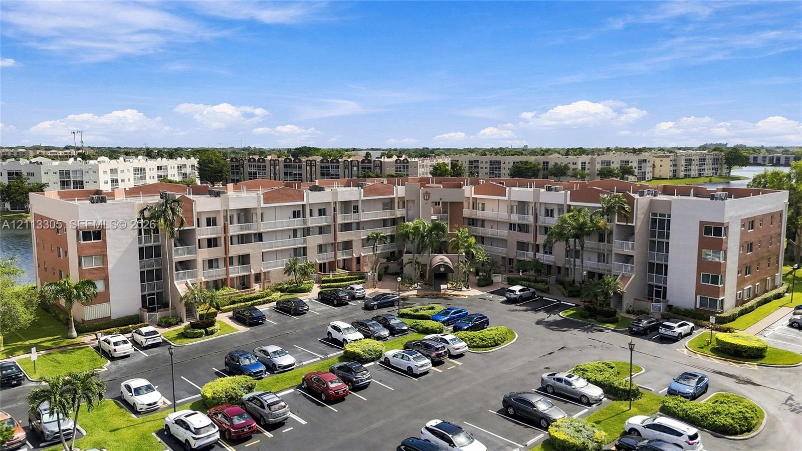 Multi-story residential complex featuring a tile roof, stucco exterior, private balconies, and landscaped grounds with mature palms