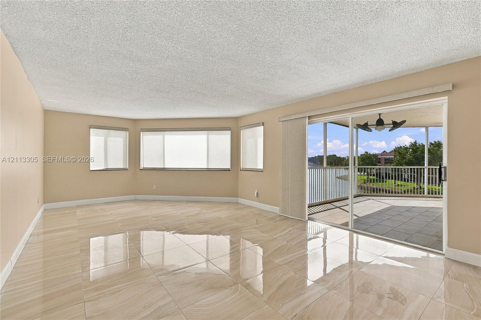 Living area featuring large-format tile flooring, expansive multi-pane windows, and a sliding glass door providing access to a screened-in balcony with ceiling fan