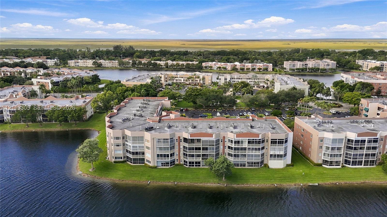 Multi-story residential complex featuring screened balconies, flat roofline, paved parking areas, and waterfront positioning