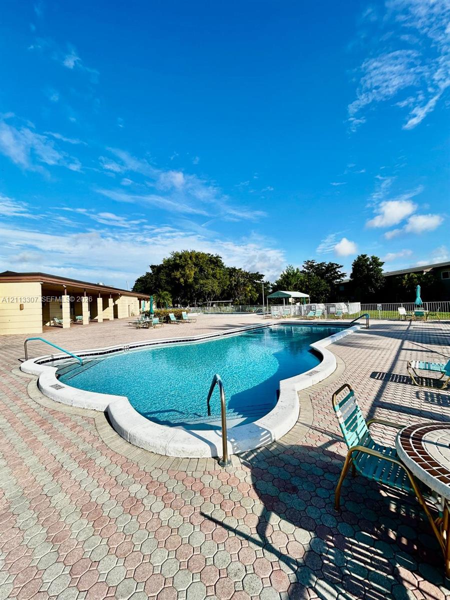 In-ground swimming pool featuring a curved concrete perimeter, metal handrails, and an expansive interlocking paver deck