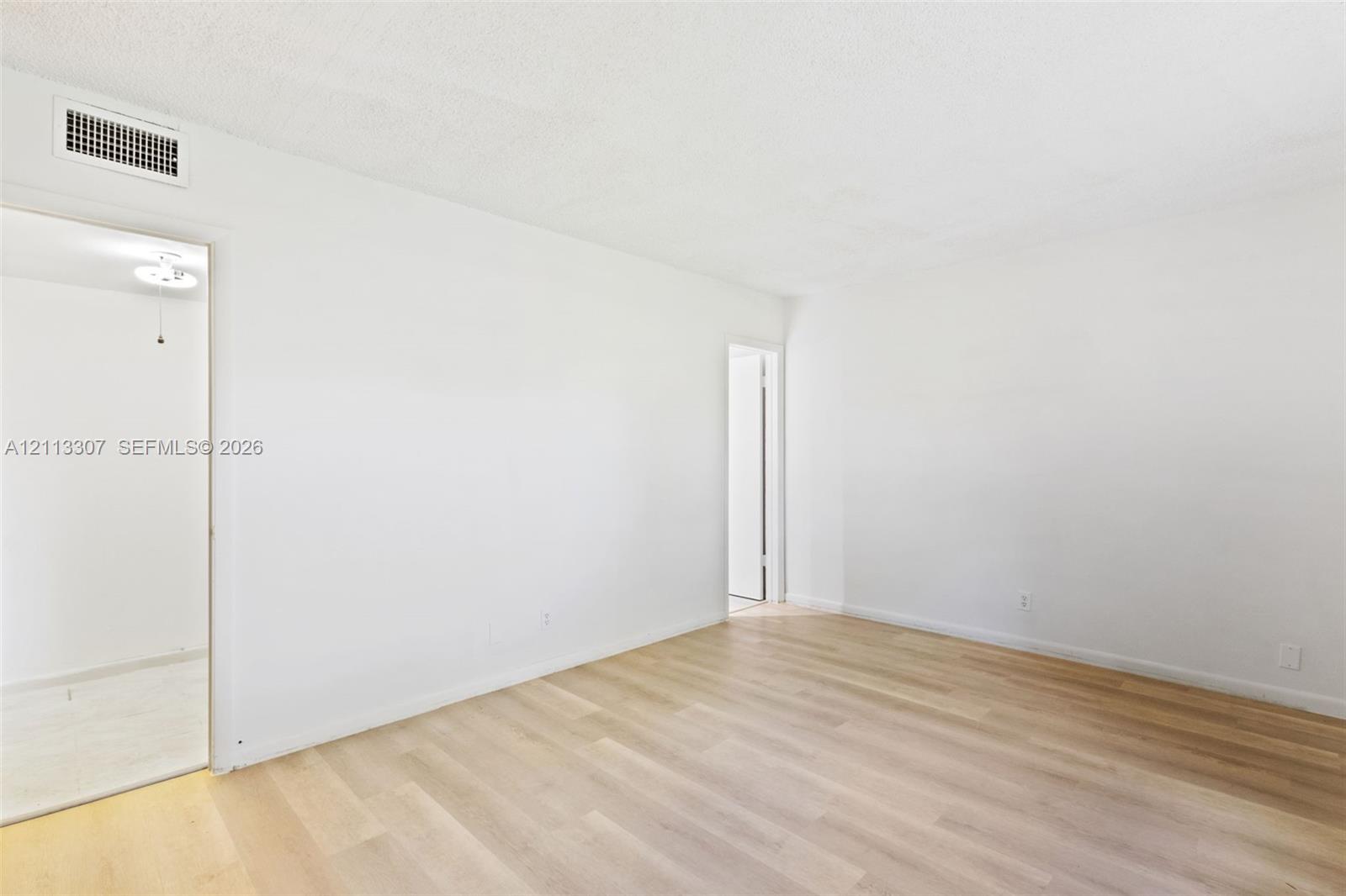 Neutral-toned living space featuring light wood-finish flooring and smooth, monochromatic walls Neutral-toned living space featuring light wood-finish flooring and smooth, monochromatic walls