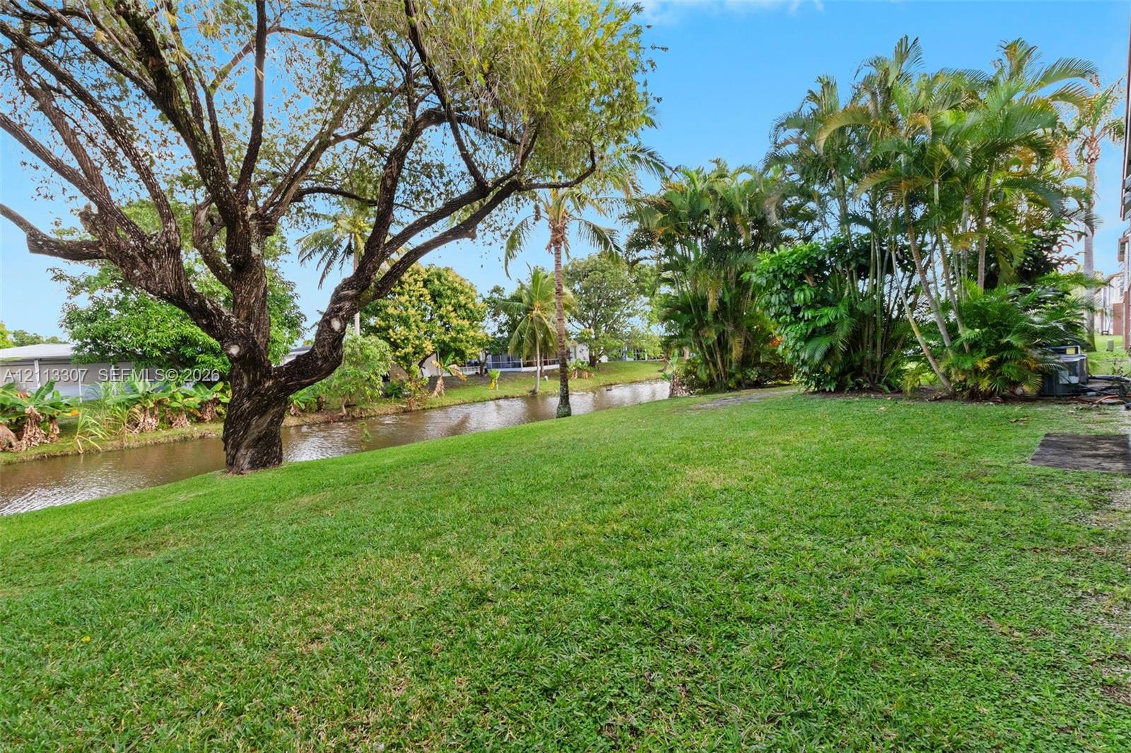 Waterfront lot featuring a grass lawn, mature trees, and established tropical vegetation