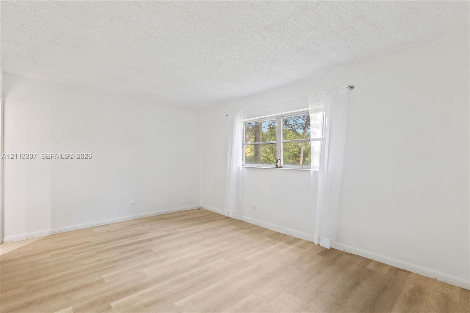 Interior room featuring wood-finish flooring, white walls, and a multi-pane window Interior room featuring wood-finish flooring, white walls, and a multi-pane window