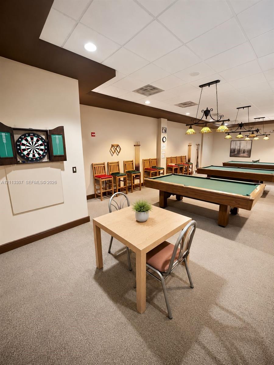 Recreation area featuring wall-mounted cabinetry, integrated billiard lighting fixtures, and a neutral carpeted floor