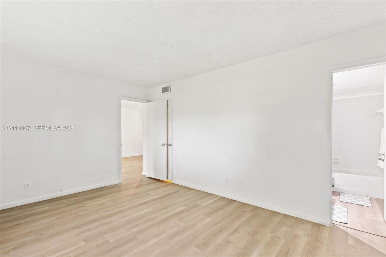 Neutral interior featuring wood-finish flooring, white walls, and a closet with double doors Neutral interior featuring wood-finish flooring, white walls, and a closet with double doors