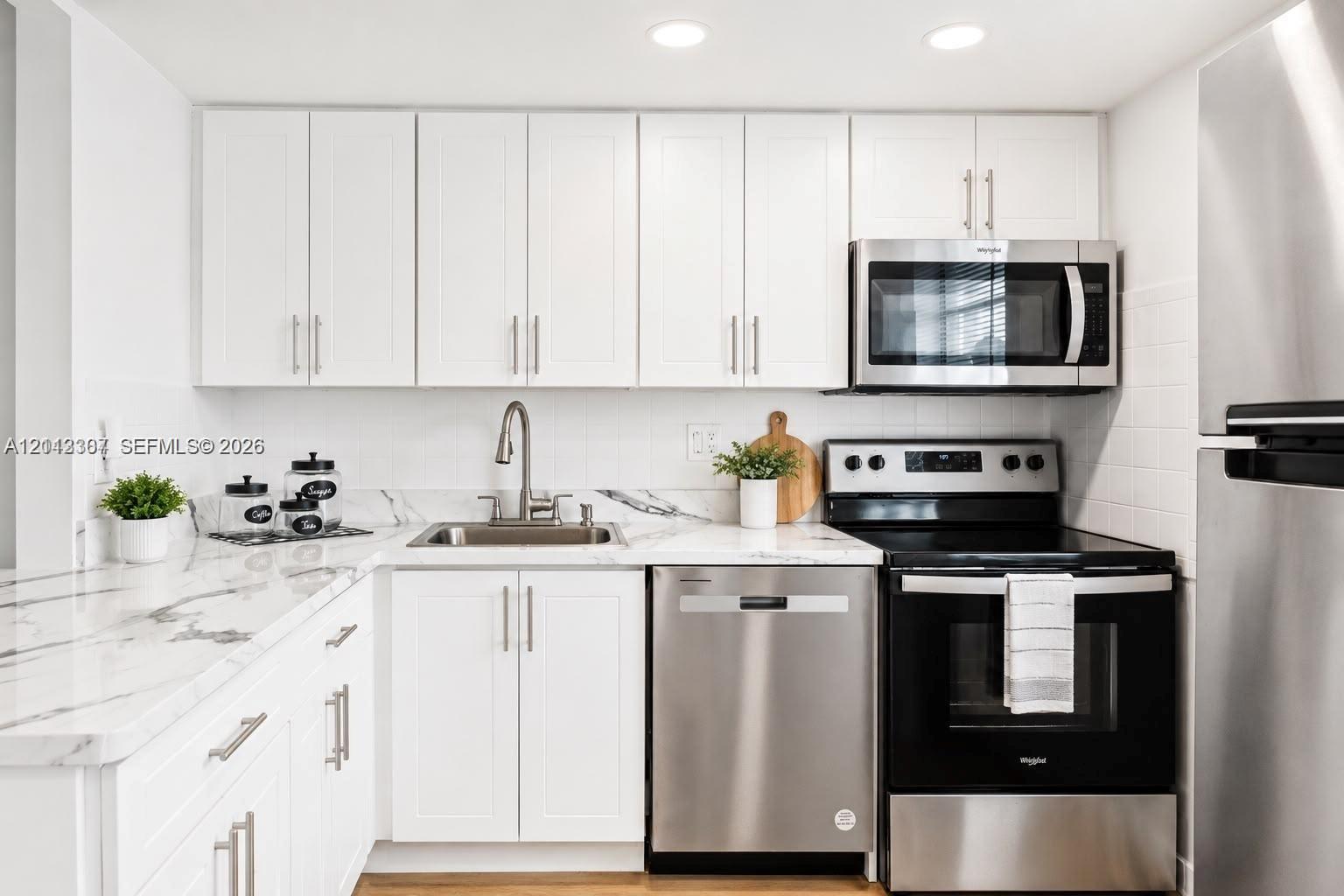 Kitchen featuring white shaker-style cabinetry, stone-patterned countertops, a white tile backsplash, stainless steel appliances, and recessed lighting