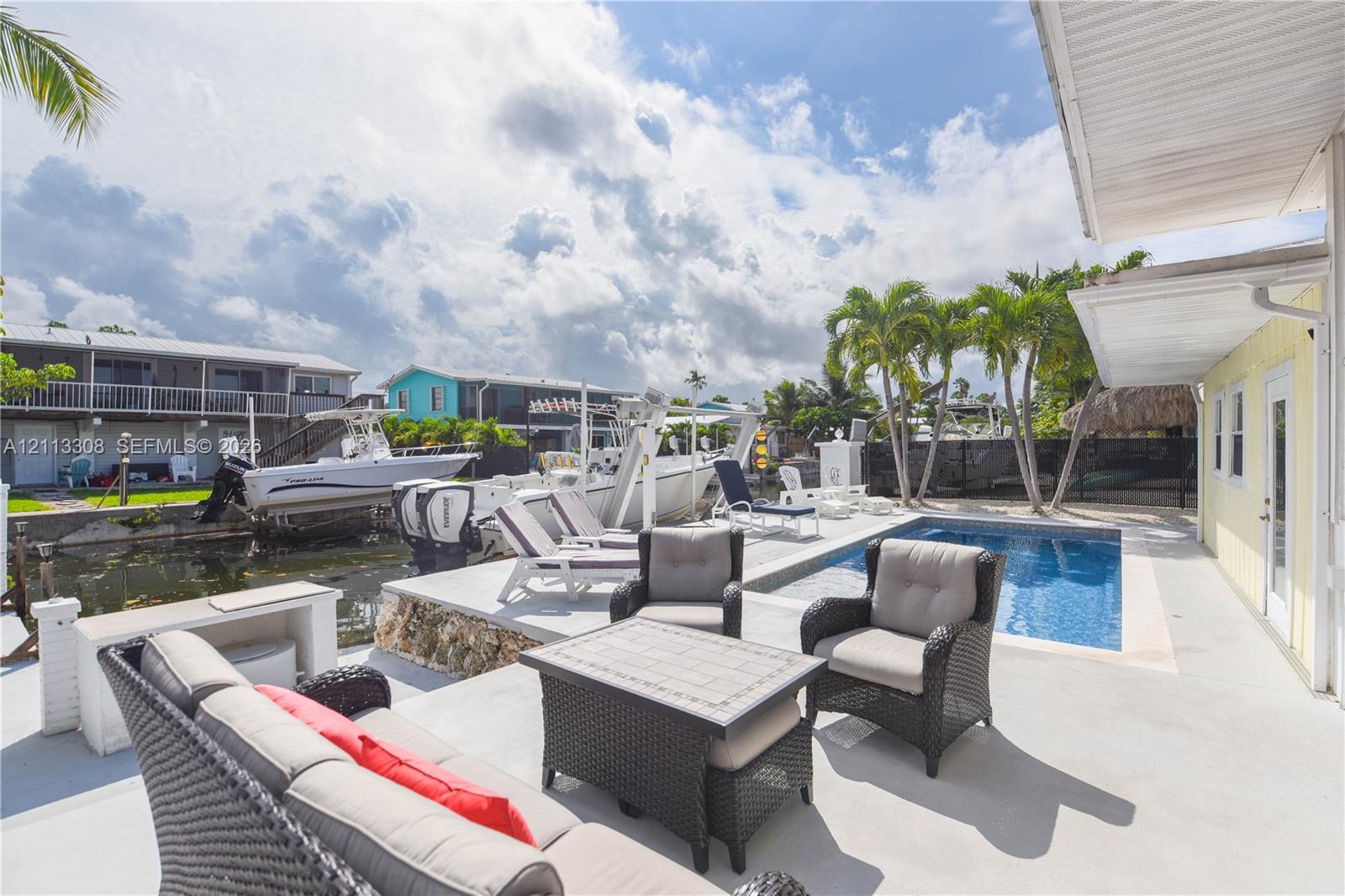 Concrete patio featuring an in-ground swimming pool, direct waterfront access with boat lift, and established palm trees