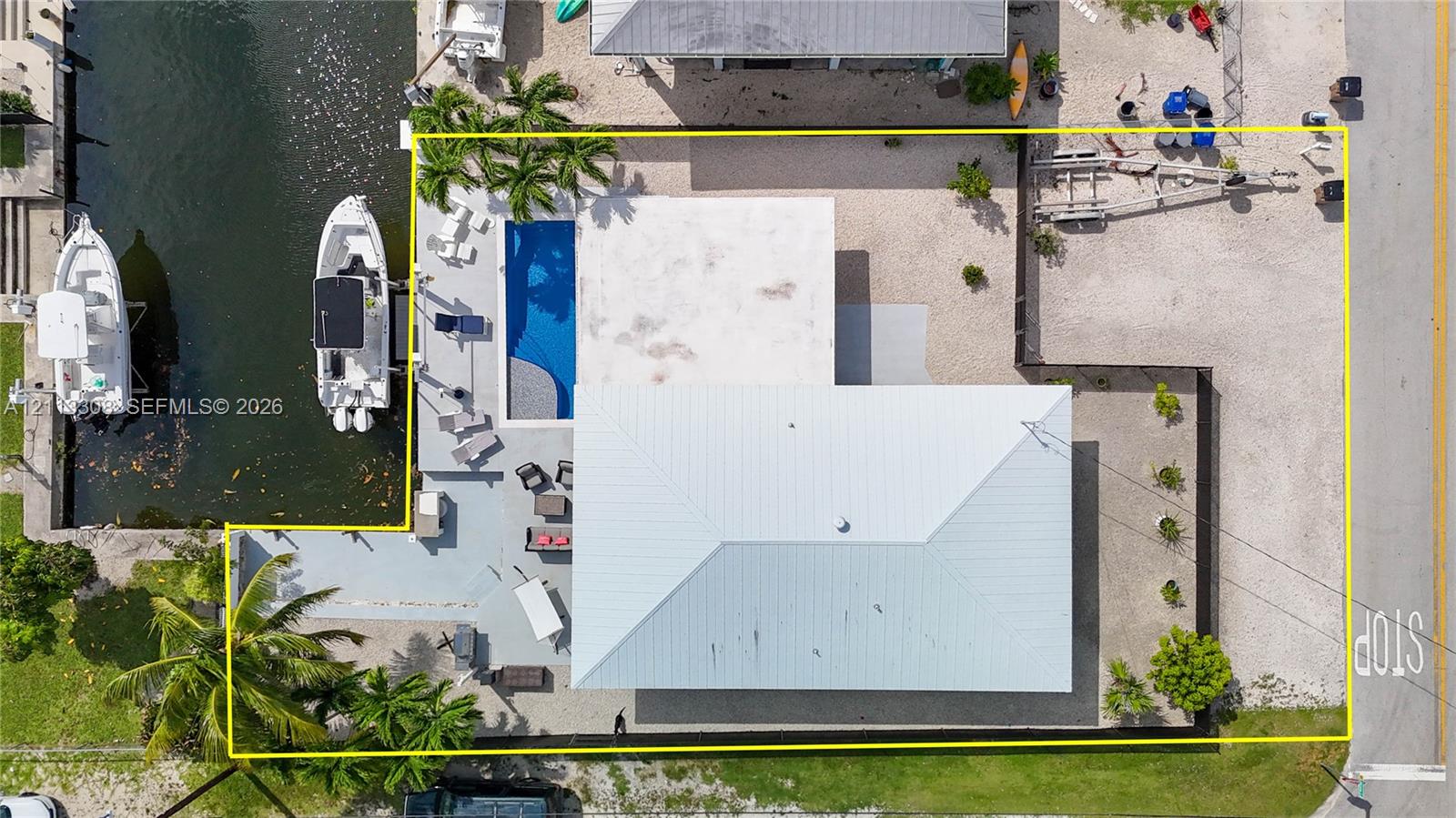 Aerial view of waterfront property featuring a canal-side bulkhead, private swimming pool, paved patio, metal roof, and gravel ground cover