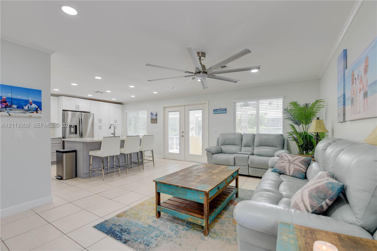 Open-concept kitchen featuring white shaker-style cabinetry, an island with seating, stainless steel appliances, recessed lighting, and tile flooring Open-concept kitchen featuring white shaker-style cabinetry, an island with seating, stainless steel appliances, recessed lighting, and tile flooring