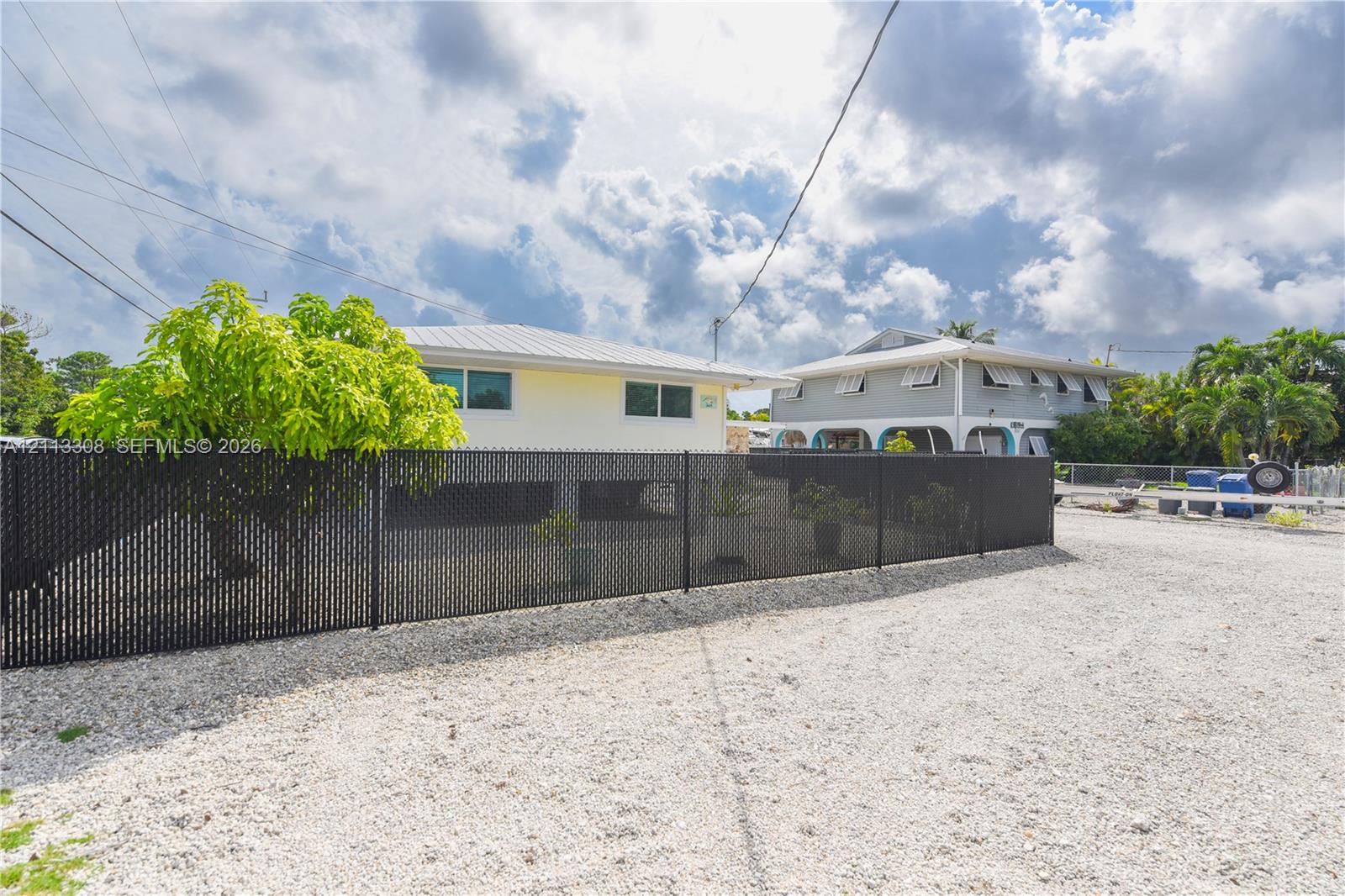 Single-story exterior featuring light-colored siding, a metal roof, and an enclosed black chain-link fence