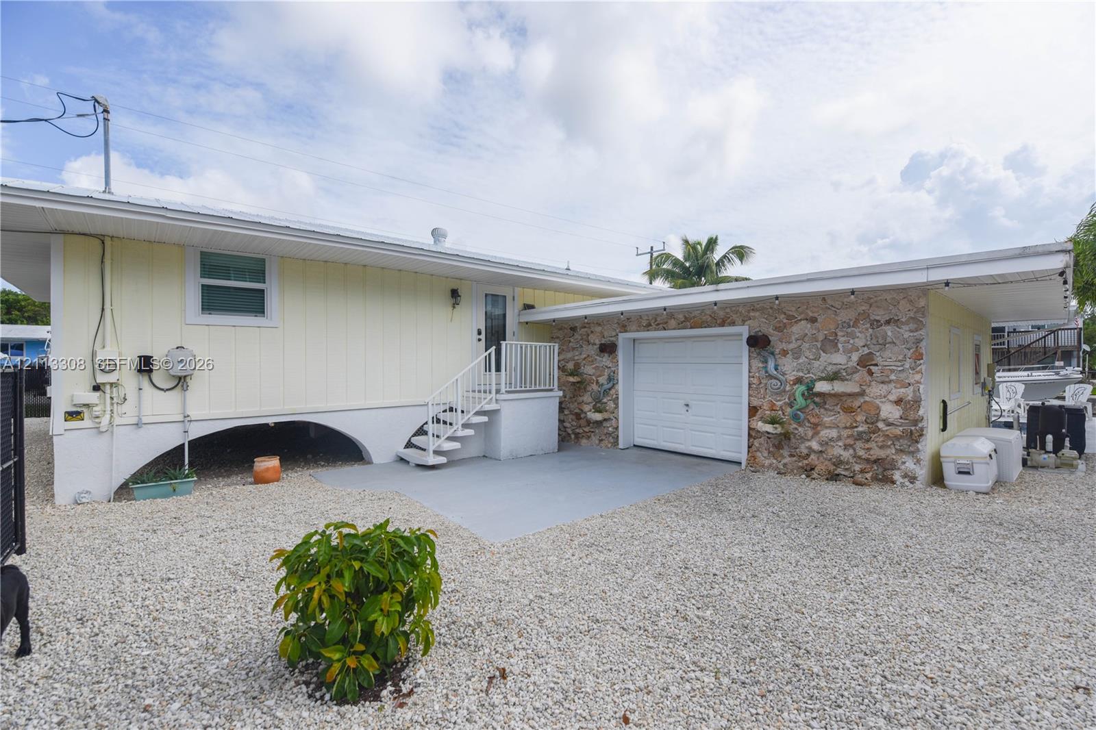 Exterior featuring natural stone masonry facade, elevated pier construction with arched supports, attached single-car garage, and gravel lot