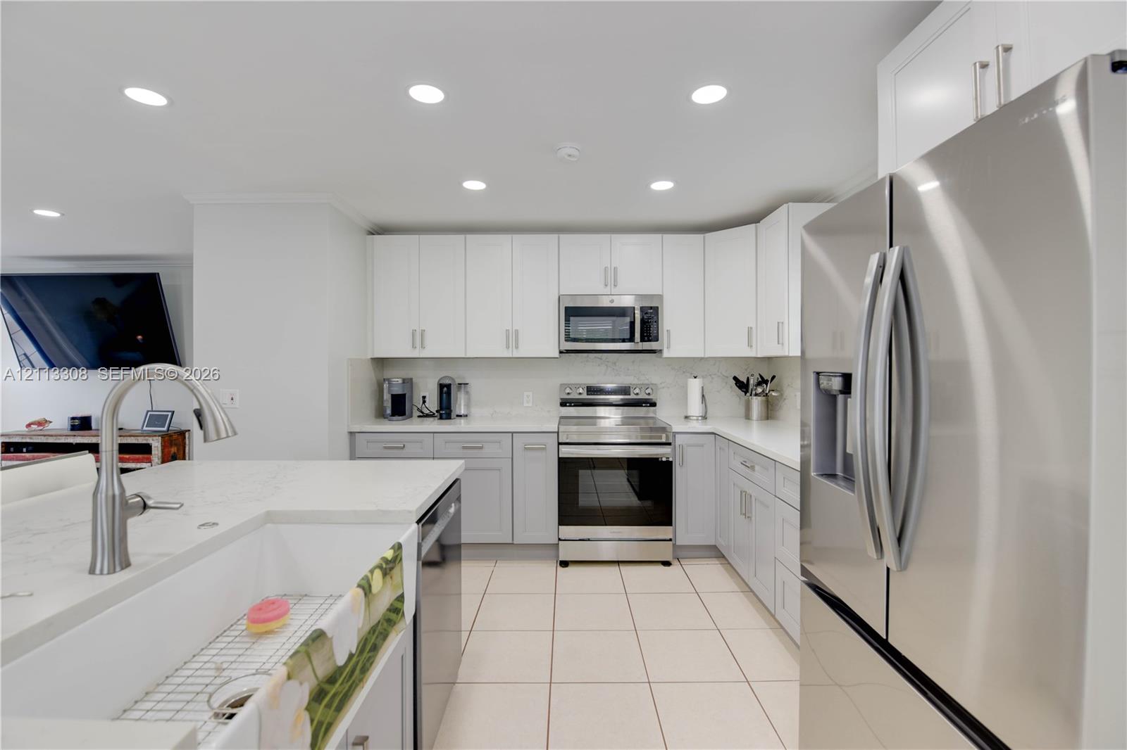 Kitchen featuring white upper cabinetry, grey lower cabinetry, stainless steel appliances, a white farmhouse sink with an arched pull-down faucet, and light-toned tile flooring