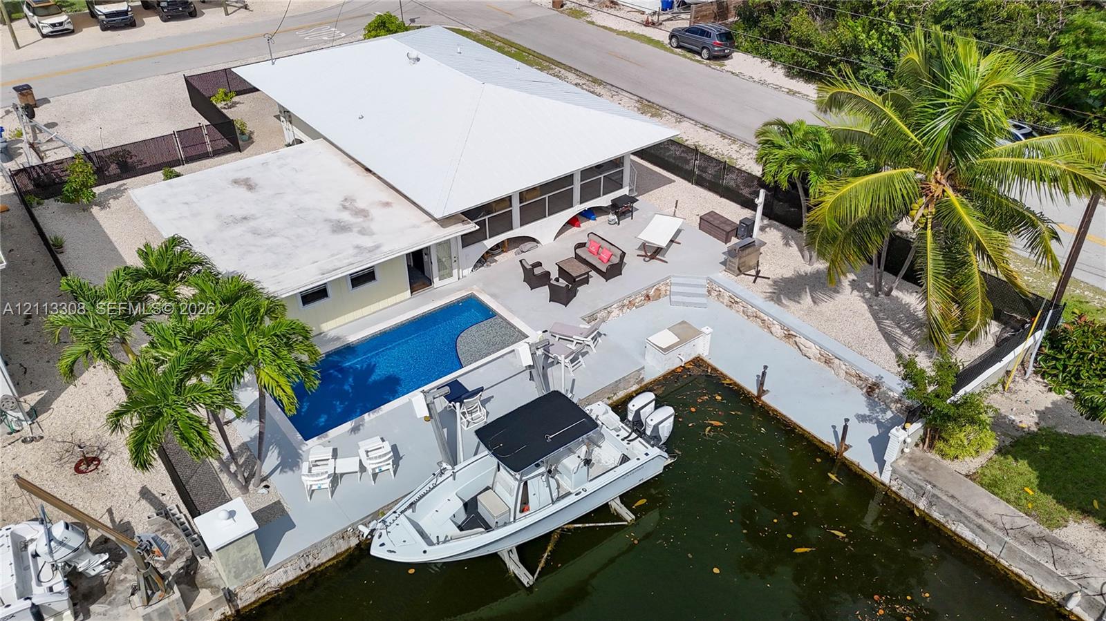 Waterfront residence featuring a private swimming pool, concrete boat slip with lift, expansive paved patio, and mature palm trees