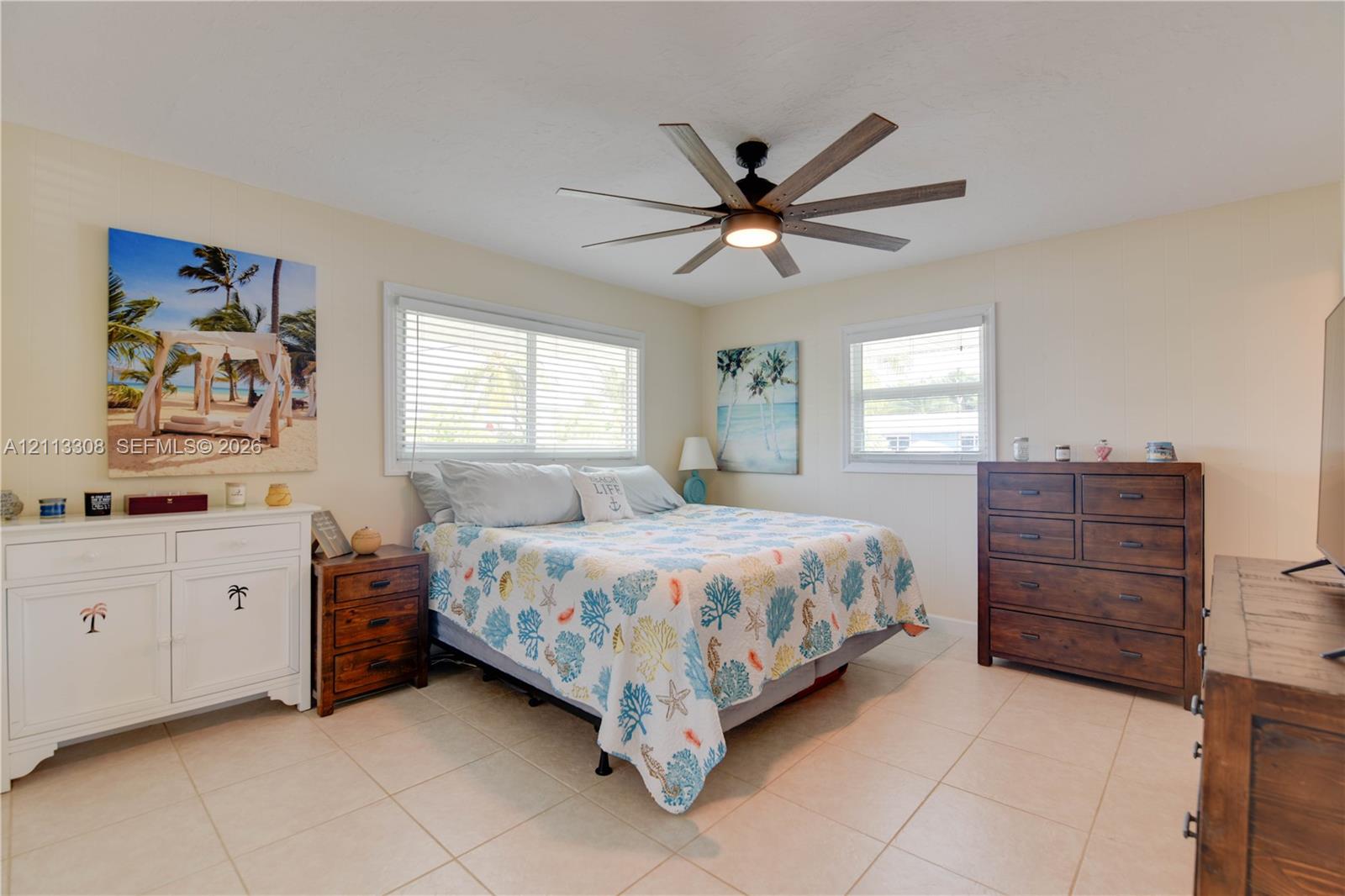 Bedroom featuring large-format tile flooring, multiple windows with blinds, and a multi-blade ceiling fan with integrated lighting Bedroom featuring large-format tile flooring, multiple windows with blinds, and a multi-blade ceiling fan with integrated lighting
