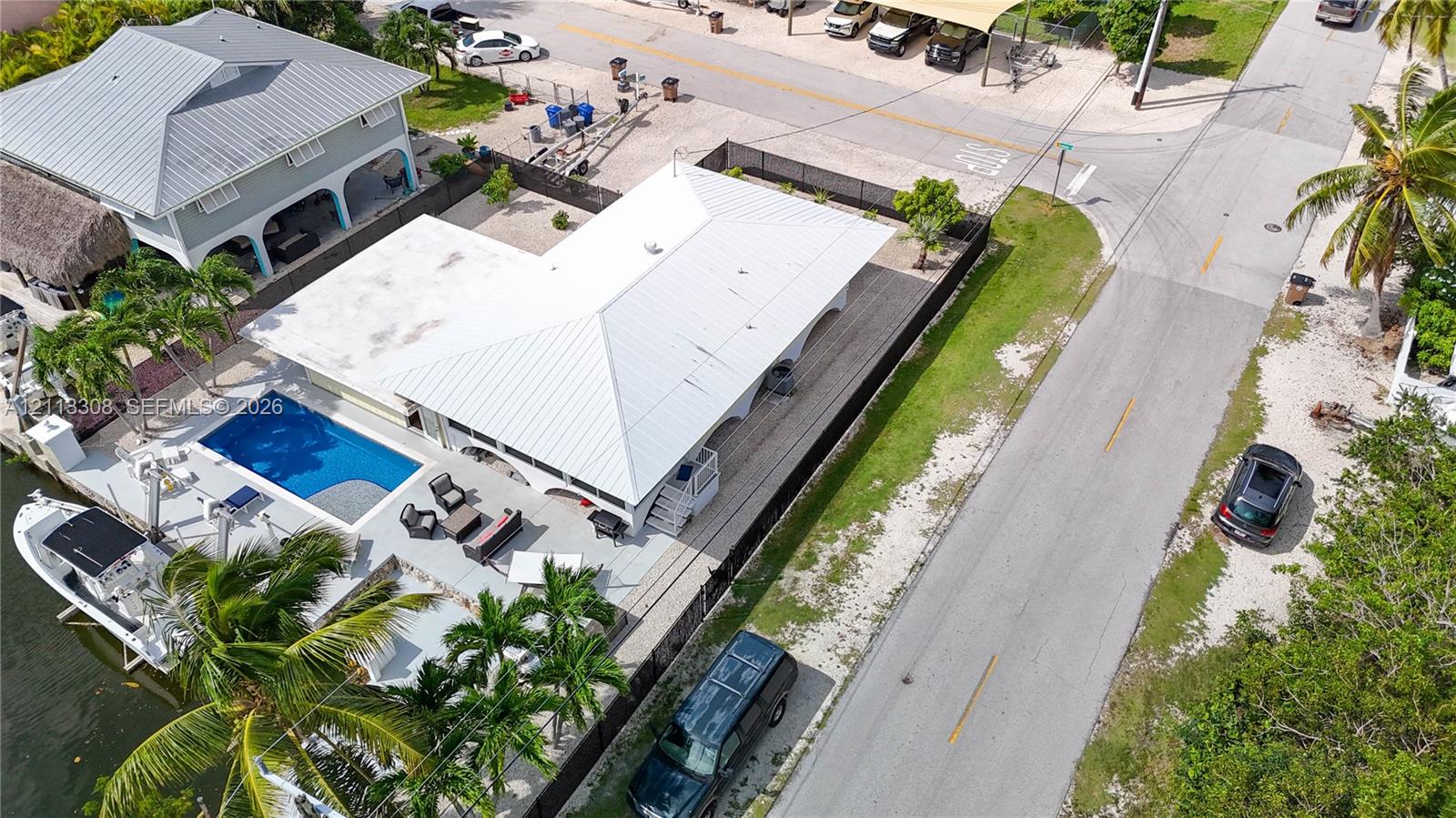 Aerial perspective of a waterfront property featuring a concrete pool deck, in-ground swimming pool, metal roof, and direct bulkhead boat docking