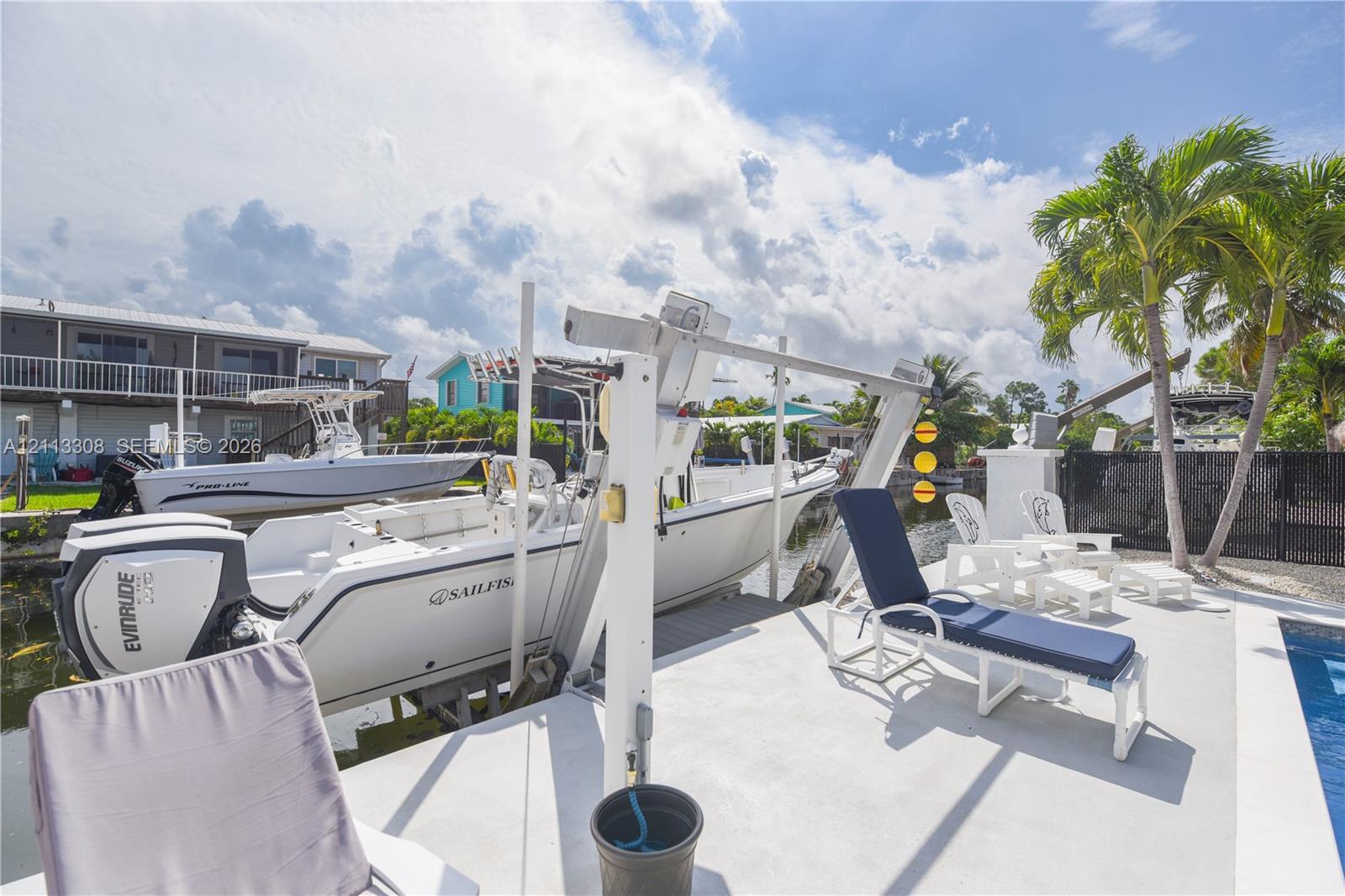 Waterfront boat lift featuring a concrete dock, swimming pool, and mature palm trees