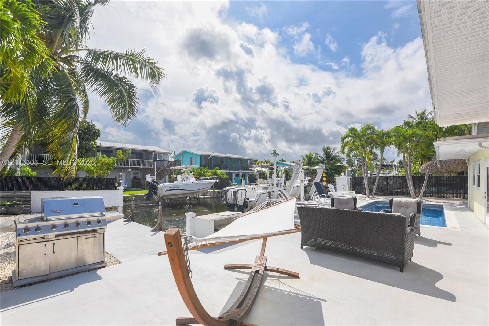 Waterfront patio featuring a swimming pool, stainless steel built-in grill, concrete deck, and private boat lift