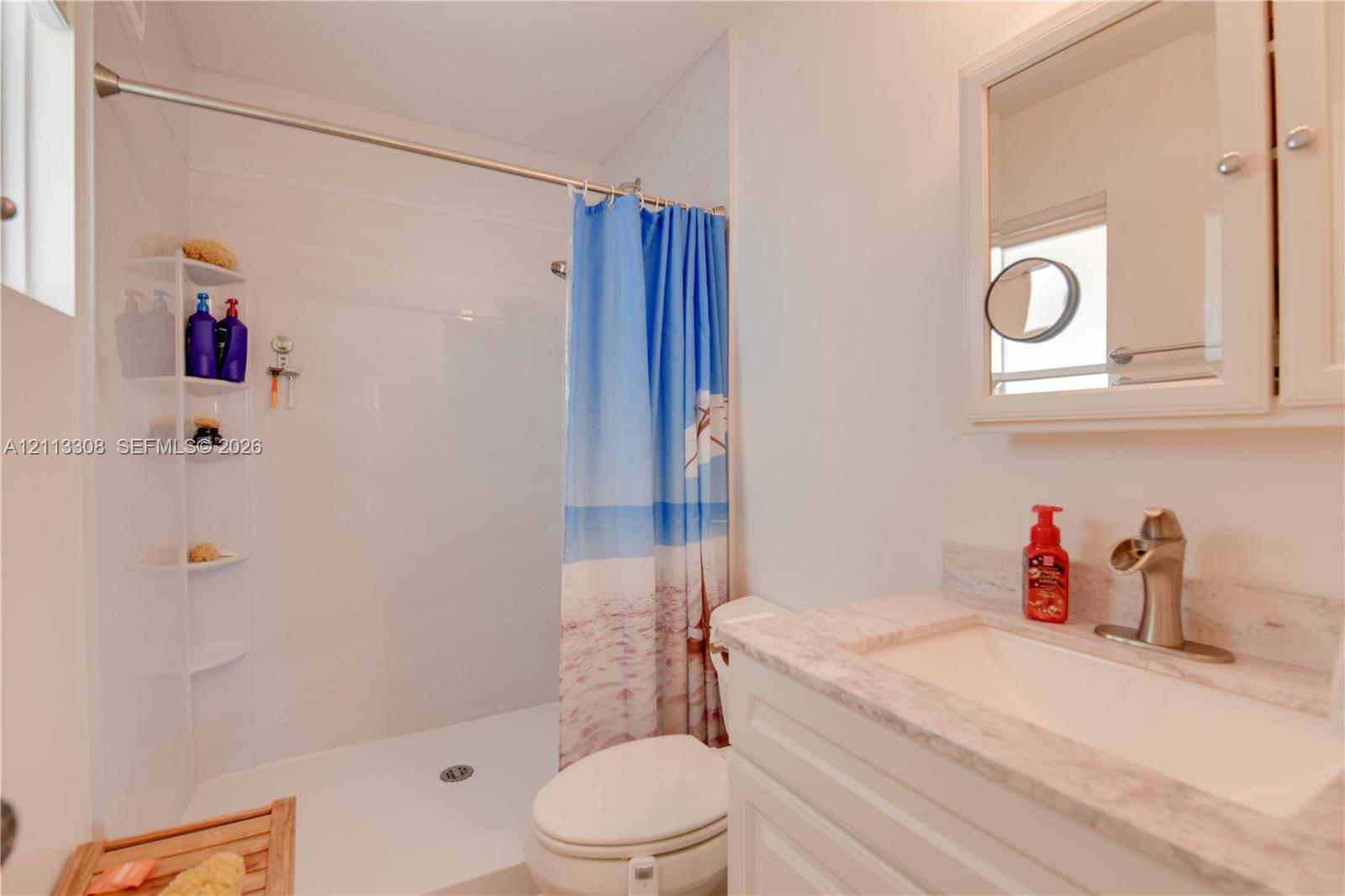 Bathroom featuring a vanity with a stone-composite countertop, integrated sink, and metallic faucet, complemented by a recessed medicine cabinet and a walk-in shower with integrated corner shelving