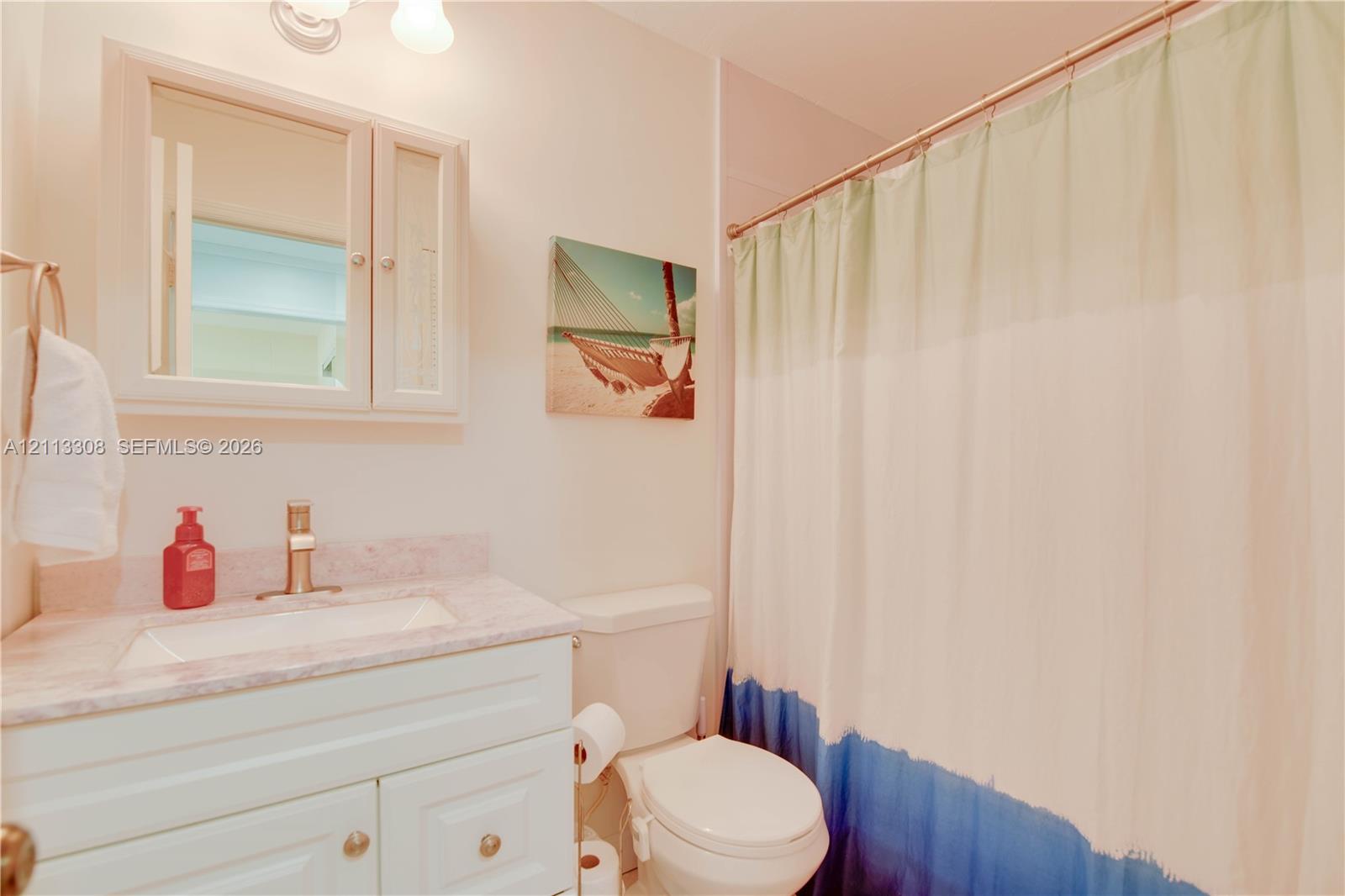 White vanity featuring a stone-composite countertop, rectangular drop-in sink, metallic faucet, wall-mounted medicine cabinet with integrated mirror, and dual-light fixture White vanity featuring a stone-composite countertop, rectangular drop-in sink, metallic faucet, wall-mounted medicine cabinet with integrated mirror, and dual-light fixture